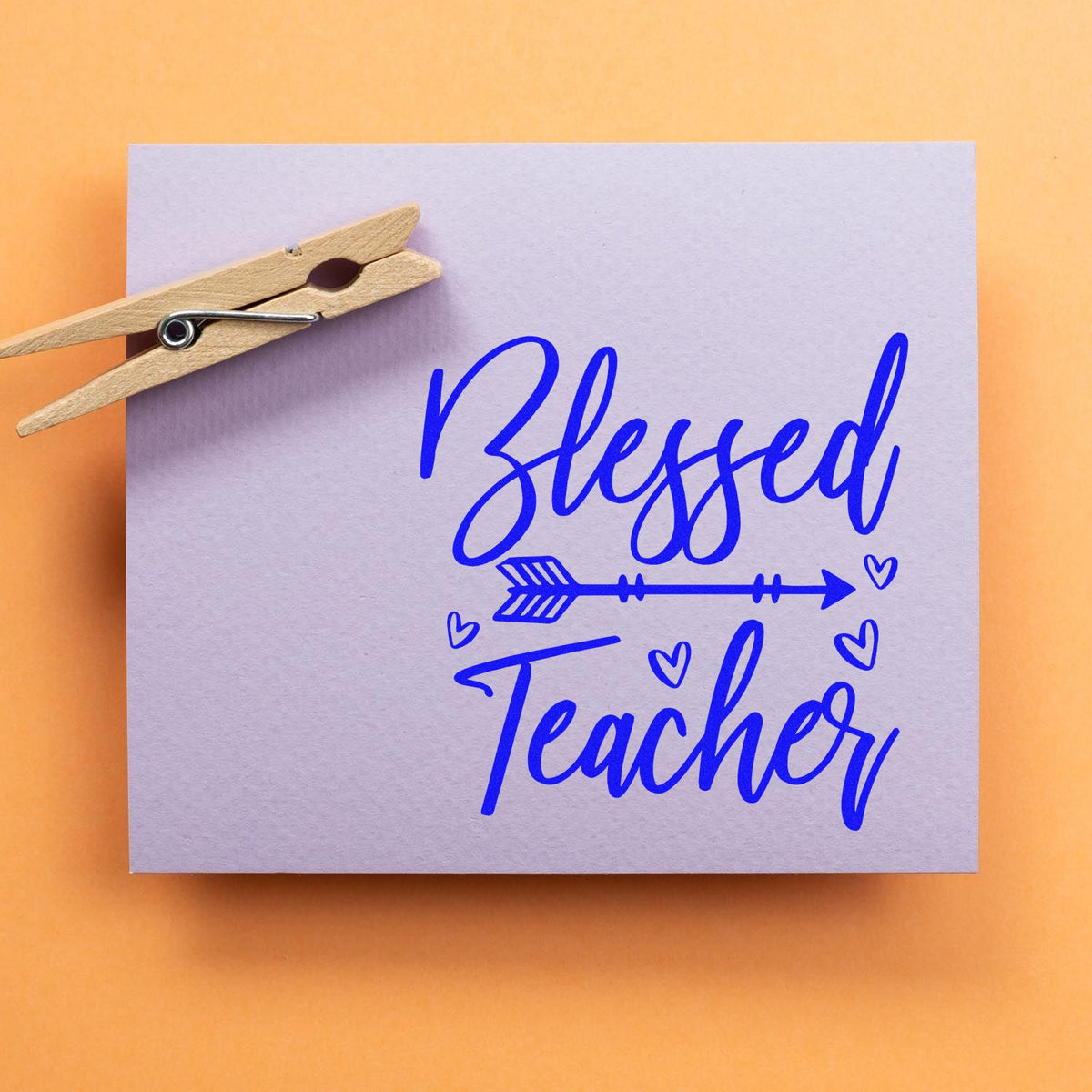 Blue Blessed Teacher stamp and seal design with hearts and arrow on lavender card, clipped by a wooden clothespin.