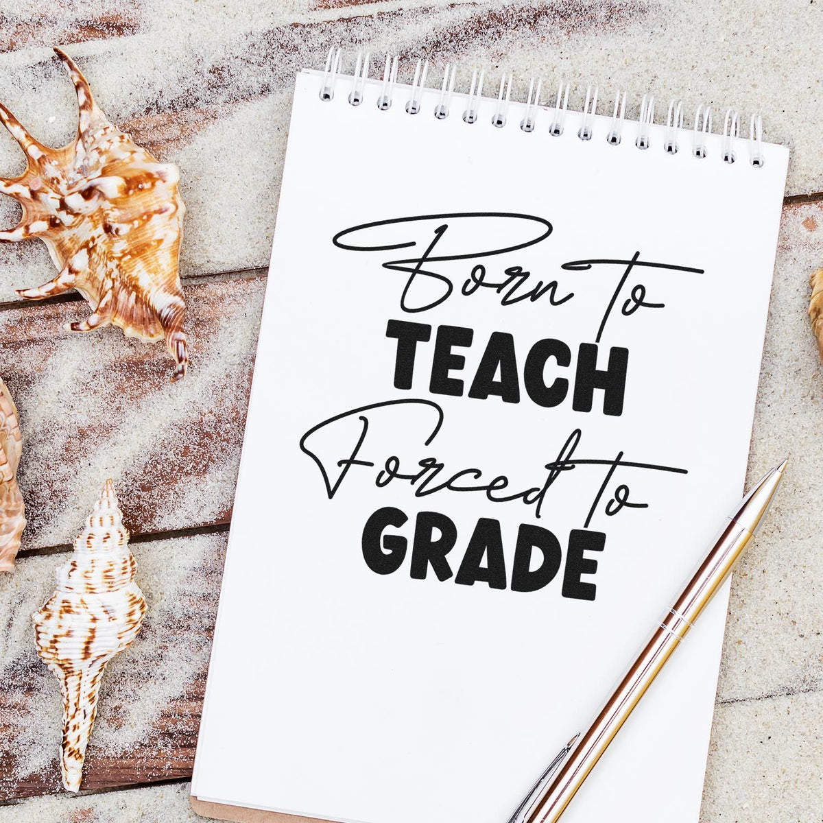 Teacher stamp and seal notebook with black Born to Teach Forced to Grade lettering, seashells, and gold pen on sandy background.