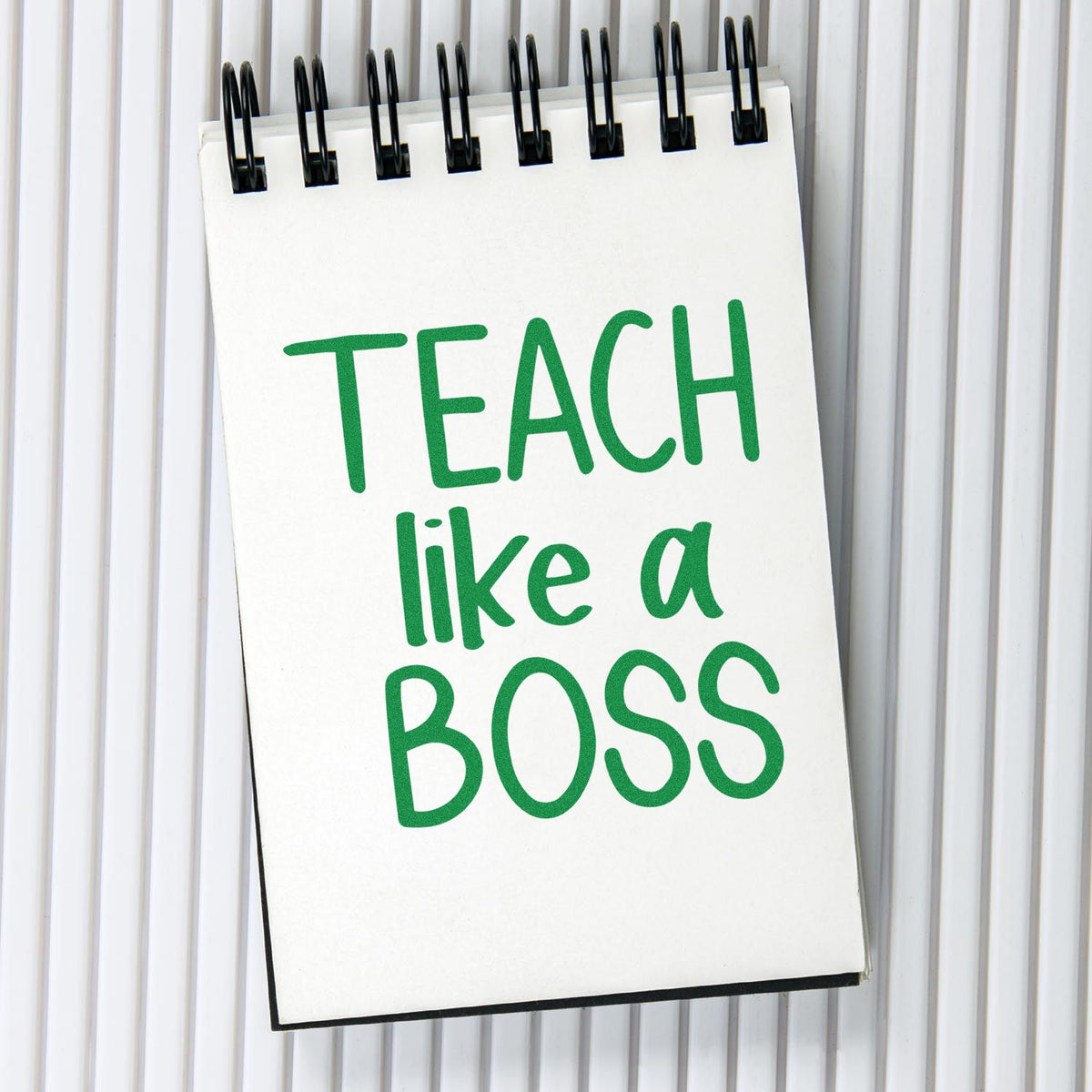White spiral-bound stamp and seal with green TEACH like a BOSS text on a gray ribbed background.