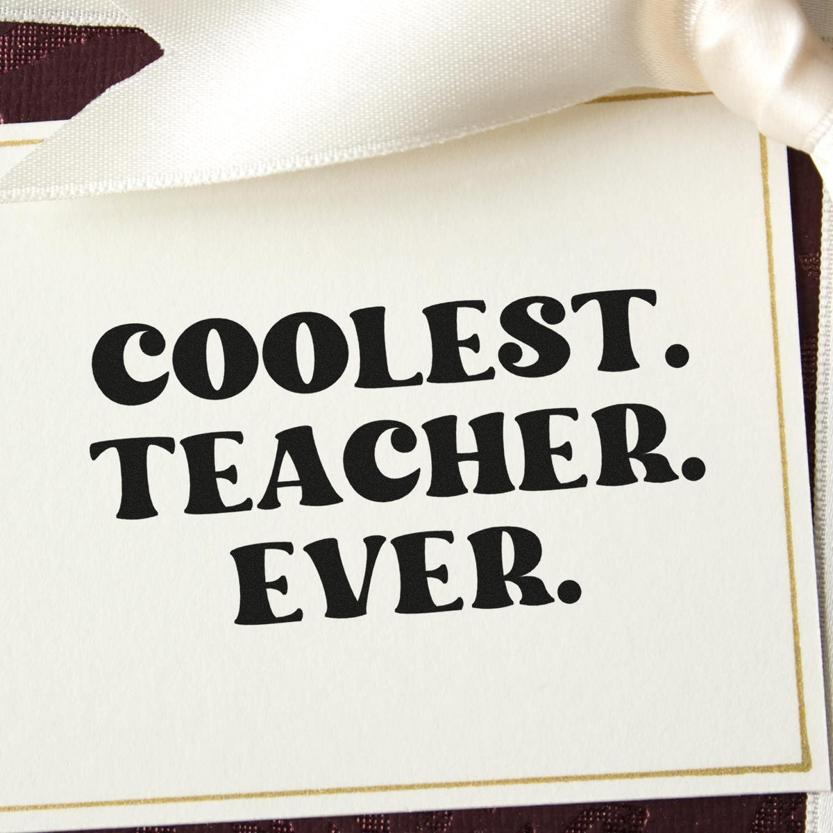 Stamp and seal product card with black COOLEST TEACHER EVER text, gold border, and cream ribbon.