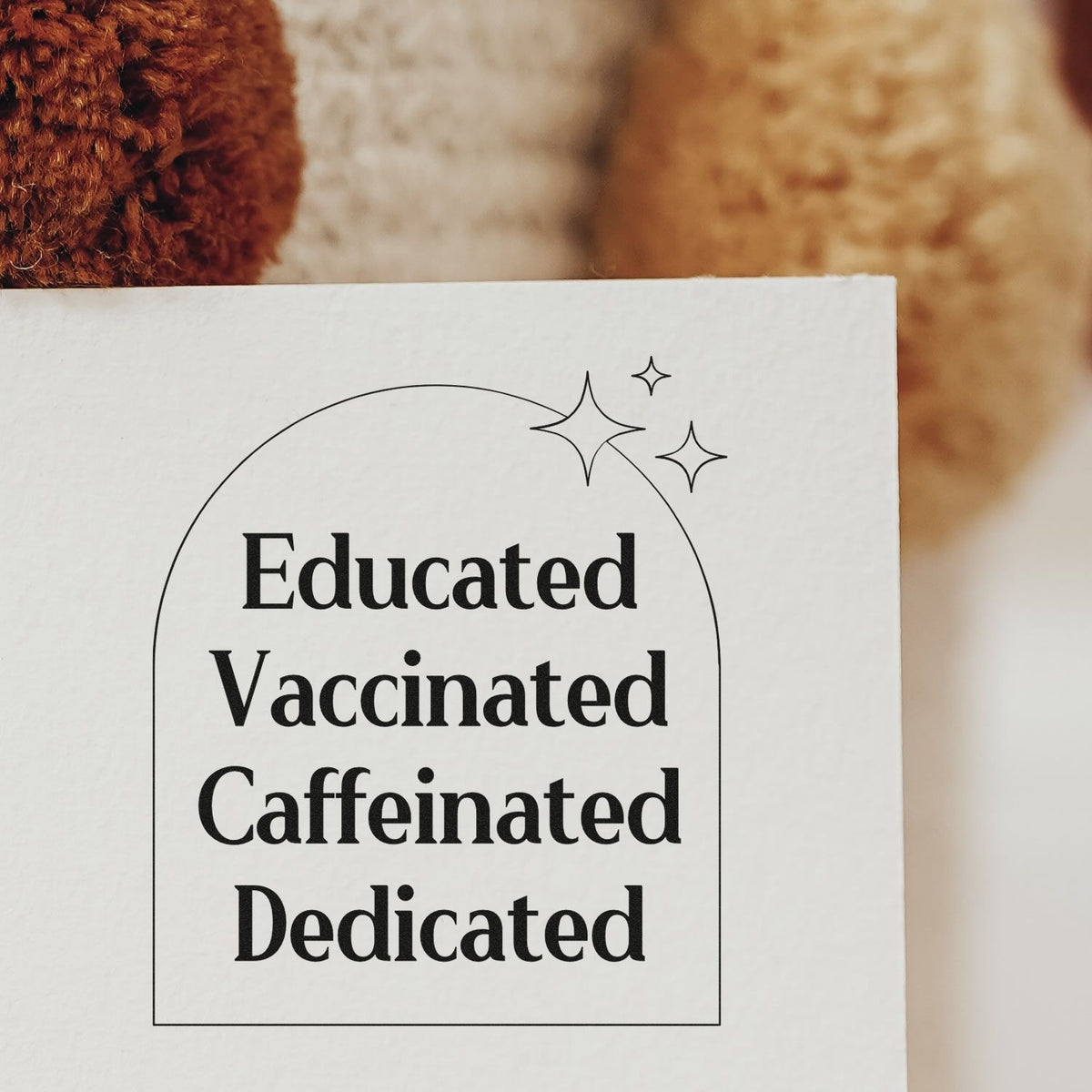 Educated Vaccinated Caffeinated Dedicated Pre-Inked Stamp – Slim imprint stamped in black ink. Four stacked words sit inside an arched outline accented by sparkles.