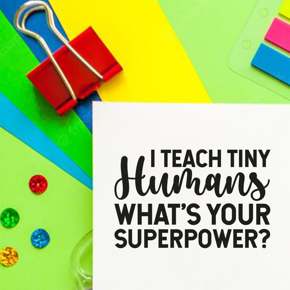 Colorful stamp and seal products with a red binder clip and white card reading I teach tiny humans whats your superpower?