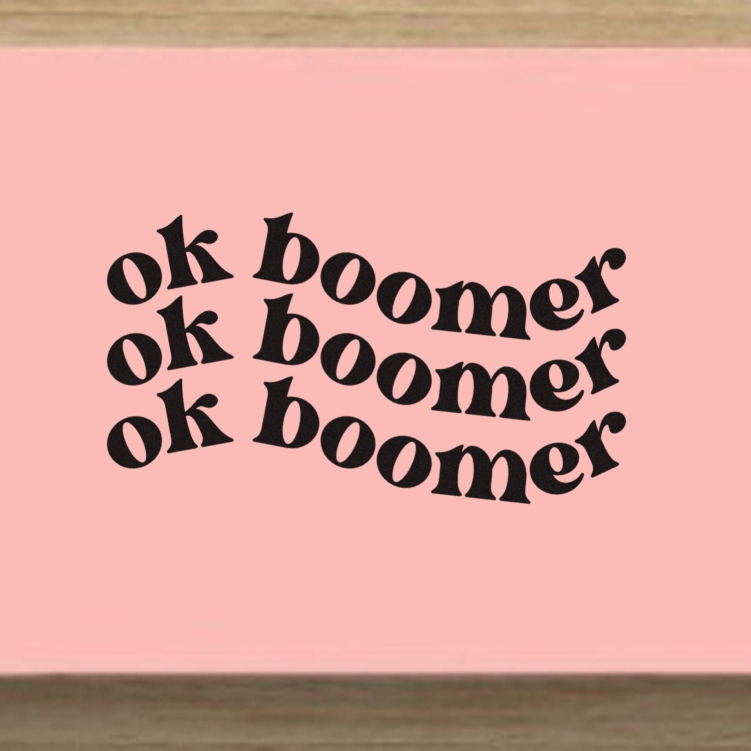 Pink stamp and seal design with bold black ok boomer text repeated in three wavy lines, retro style.