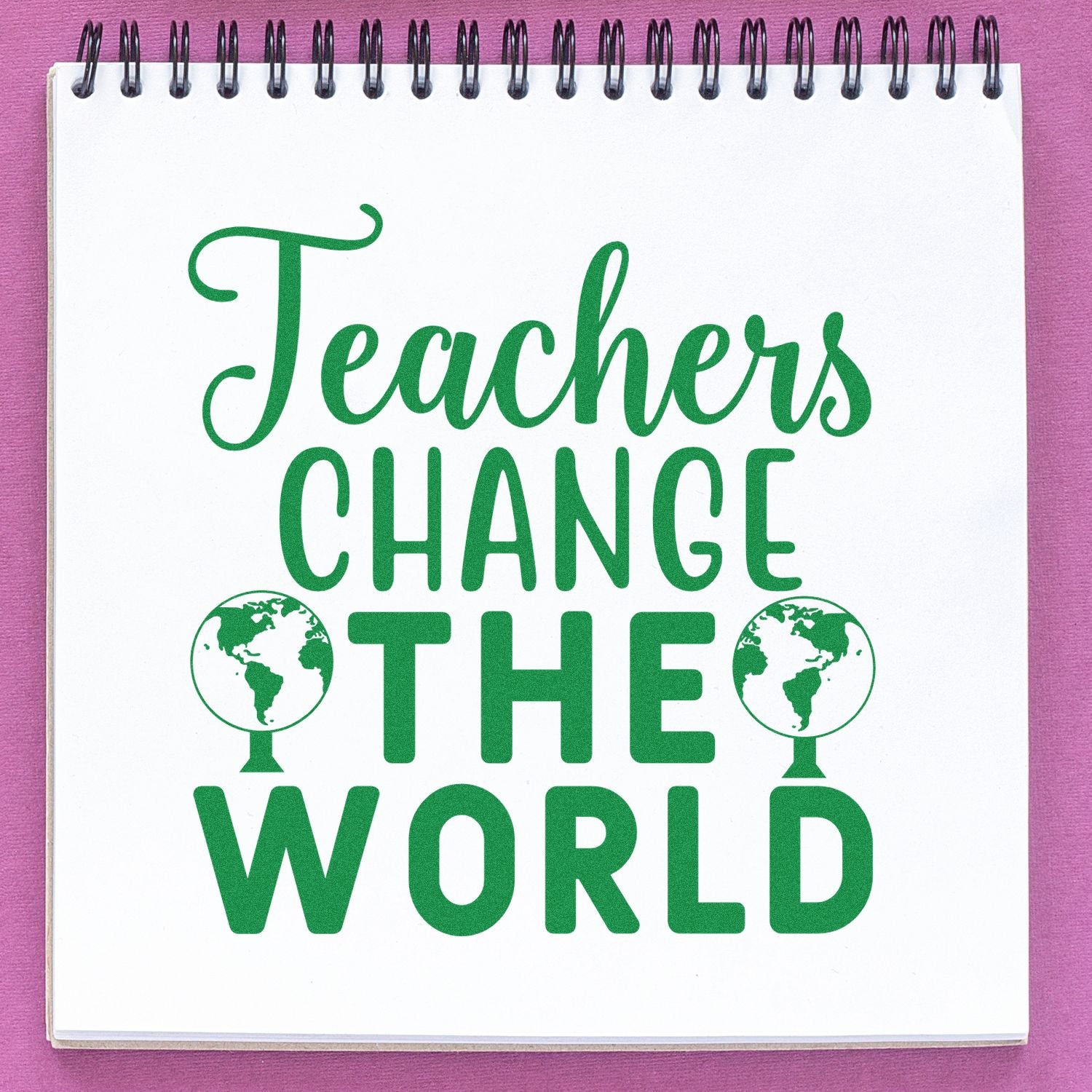 Green teacher stamp seal reading CHANGE THE WORLD on a white spiral notebook with pink background.