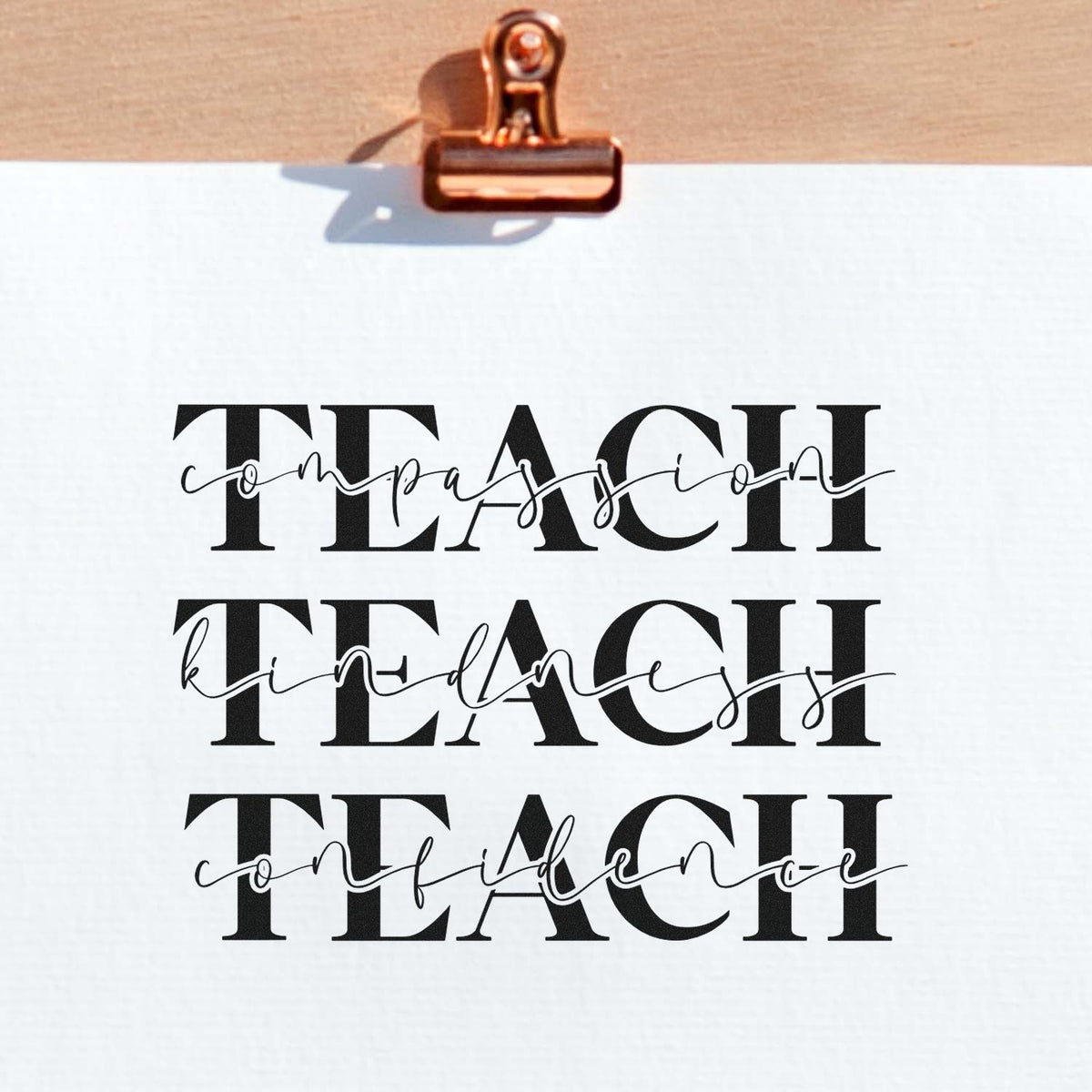 Copper binder clip holding white sheet with black TEACH stamp and seal designs: compassion, kindness, confidence.