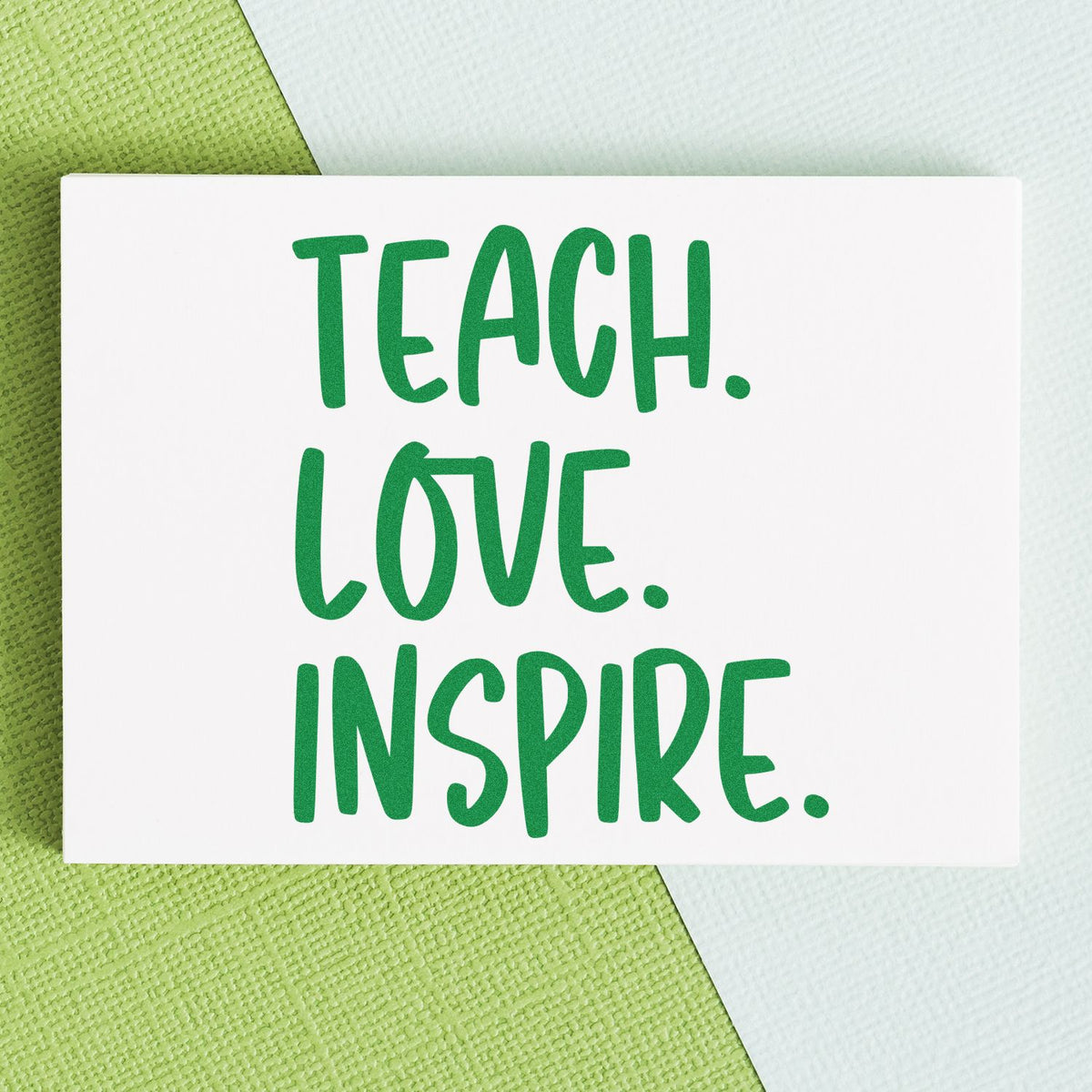 White rubber stamp card with green TEACH. LOVE. INSPIRE. text on green and white textured background.
