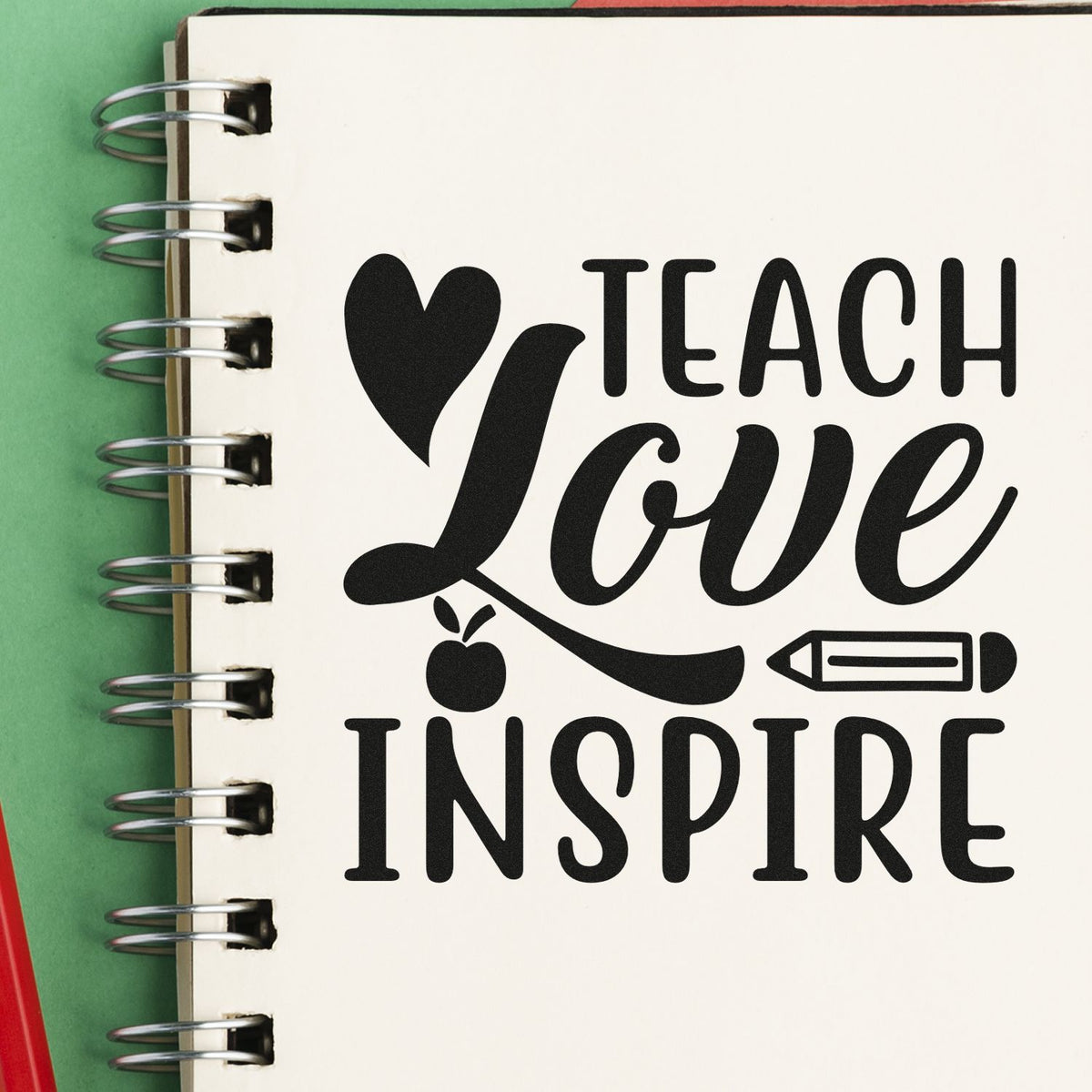 Black teacher stamp and seal design with heart, apple and pencil on a cream spiral notebook against a green background