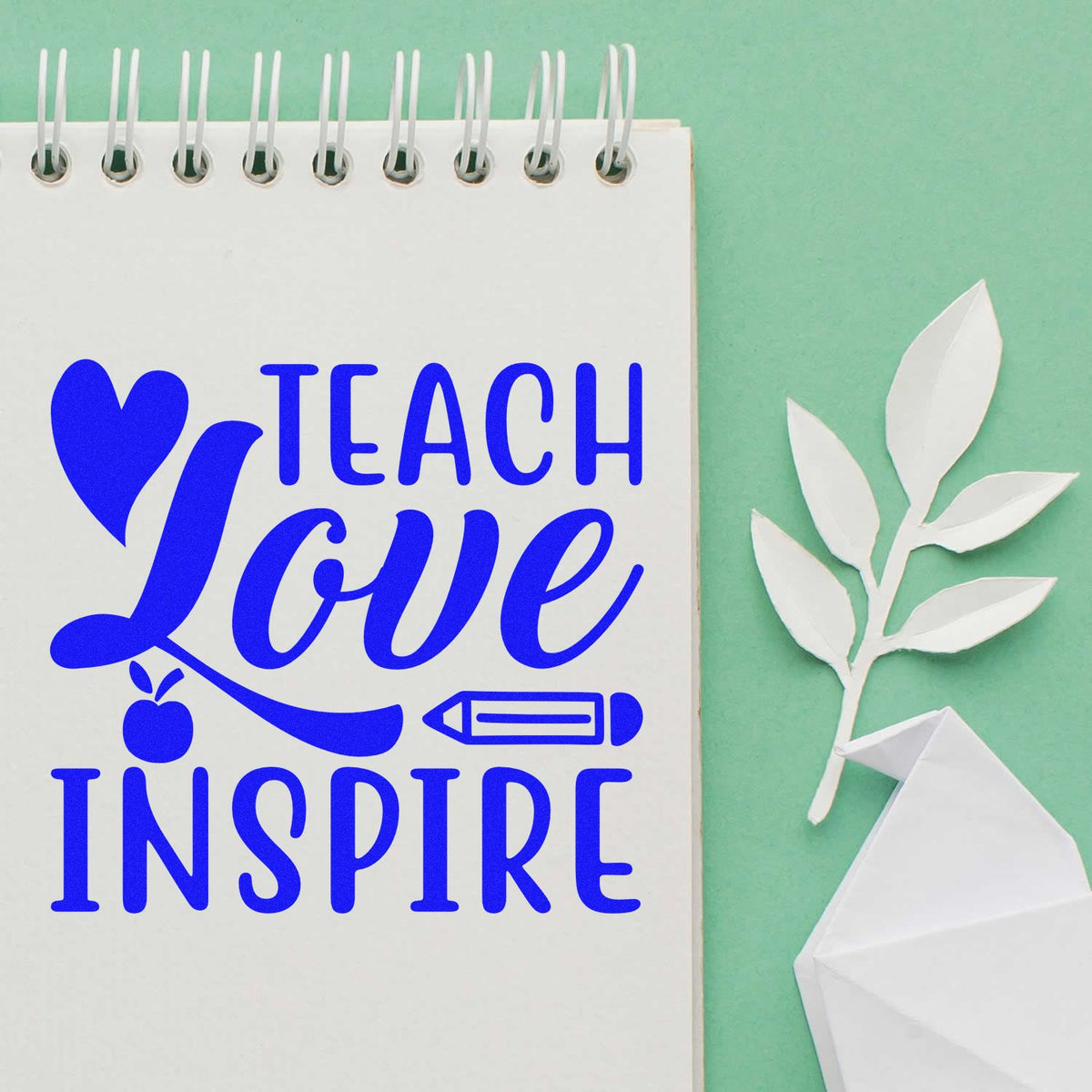 Blue Teach Love Inspire stamp and folded paper seal on spiral notebook, with white leaves on mint green background