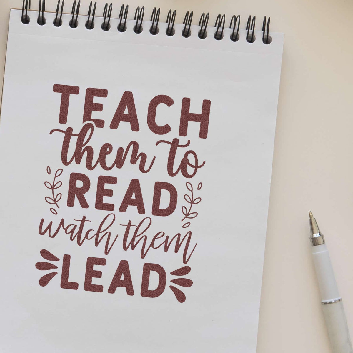 Maroon teacher stamp and seal design on white spiral notebook: Teach them to read, watch them lead with leaf accents.
