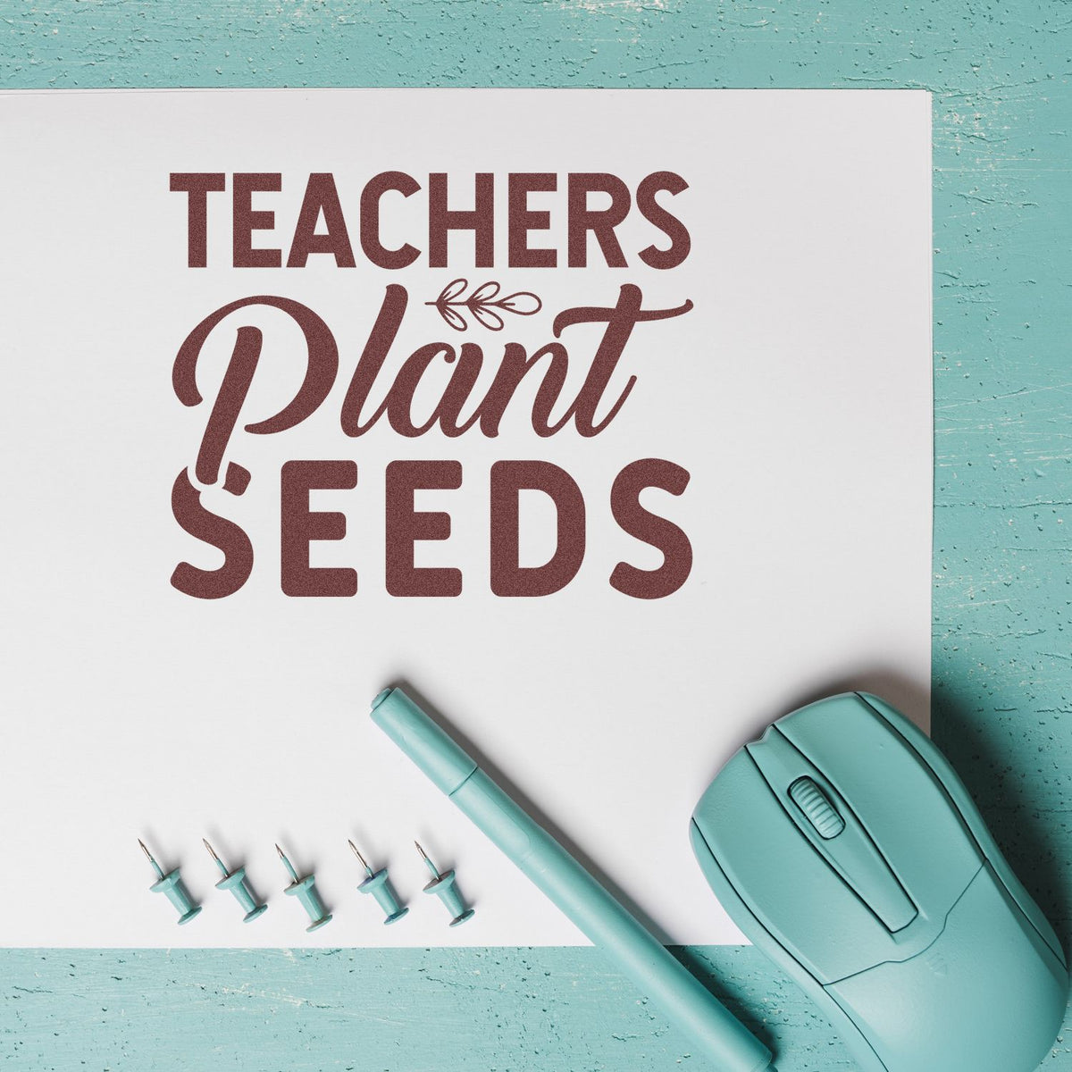 Teal stamp and seal set with maroon Teachers Plant Seeds design, matching pen, pins, and mouse on white sheet.