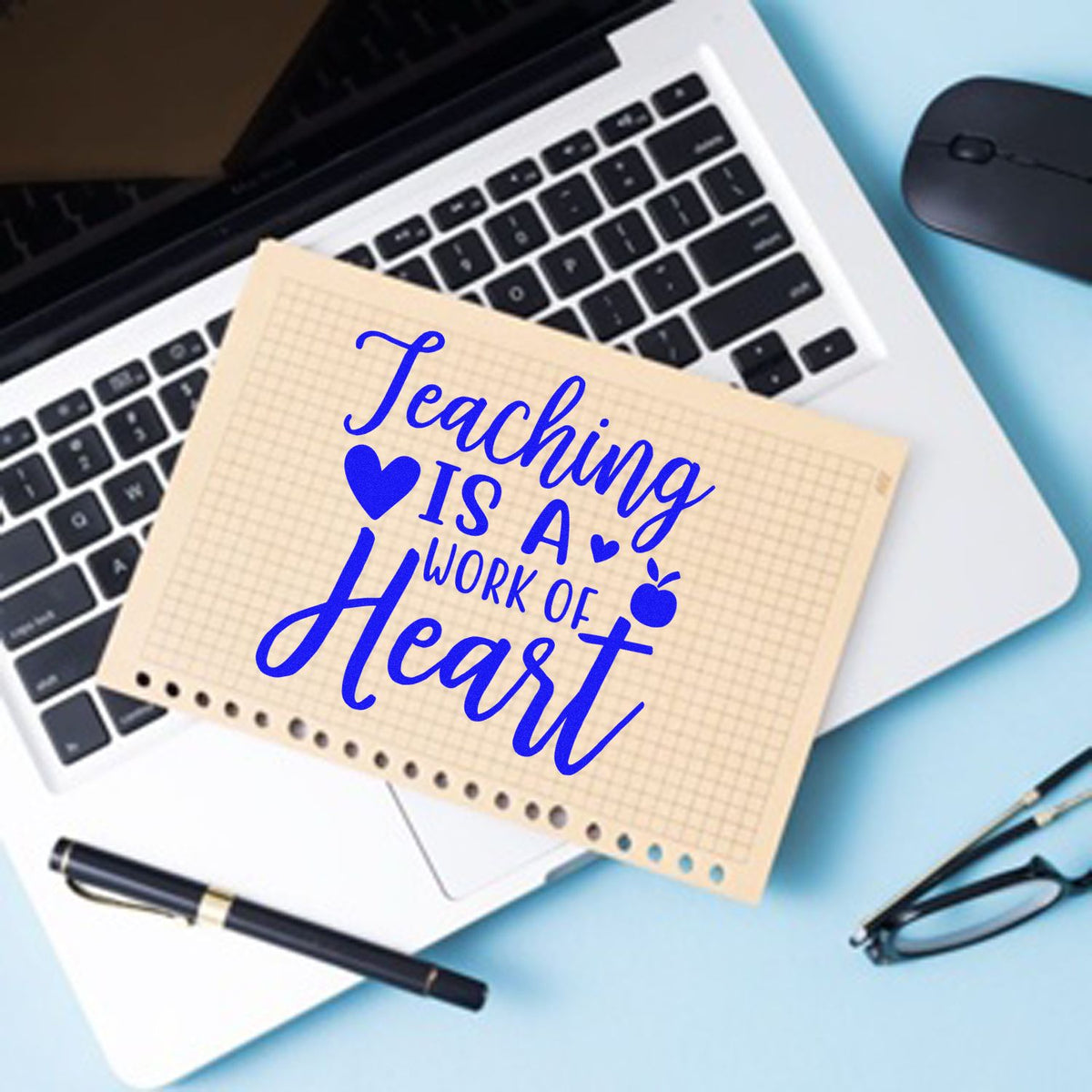 Blue teaching rubber stamp on beige grid paper over laptop keyboard, with pen, glasses and mouse.