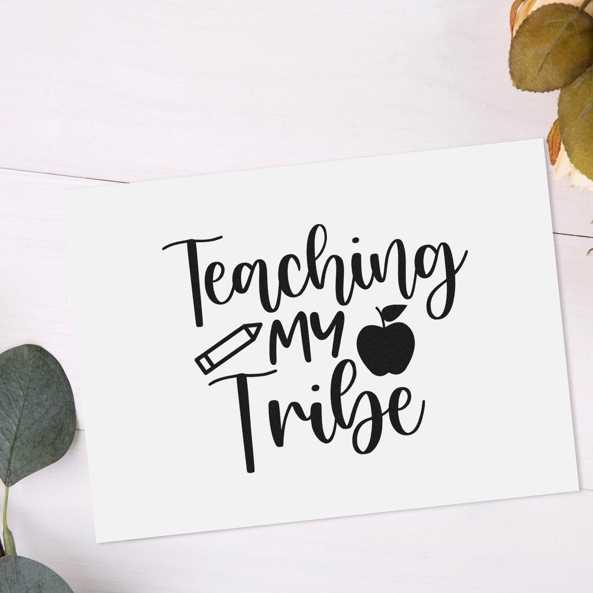 Black teaching-themed stamp seal reading Teaching My Tribe with pencil and apple on white card, accented by green leaves.