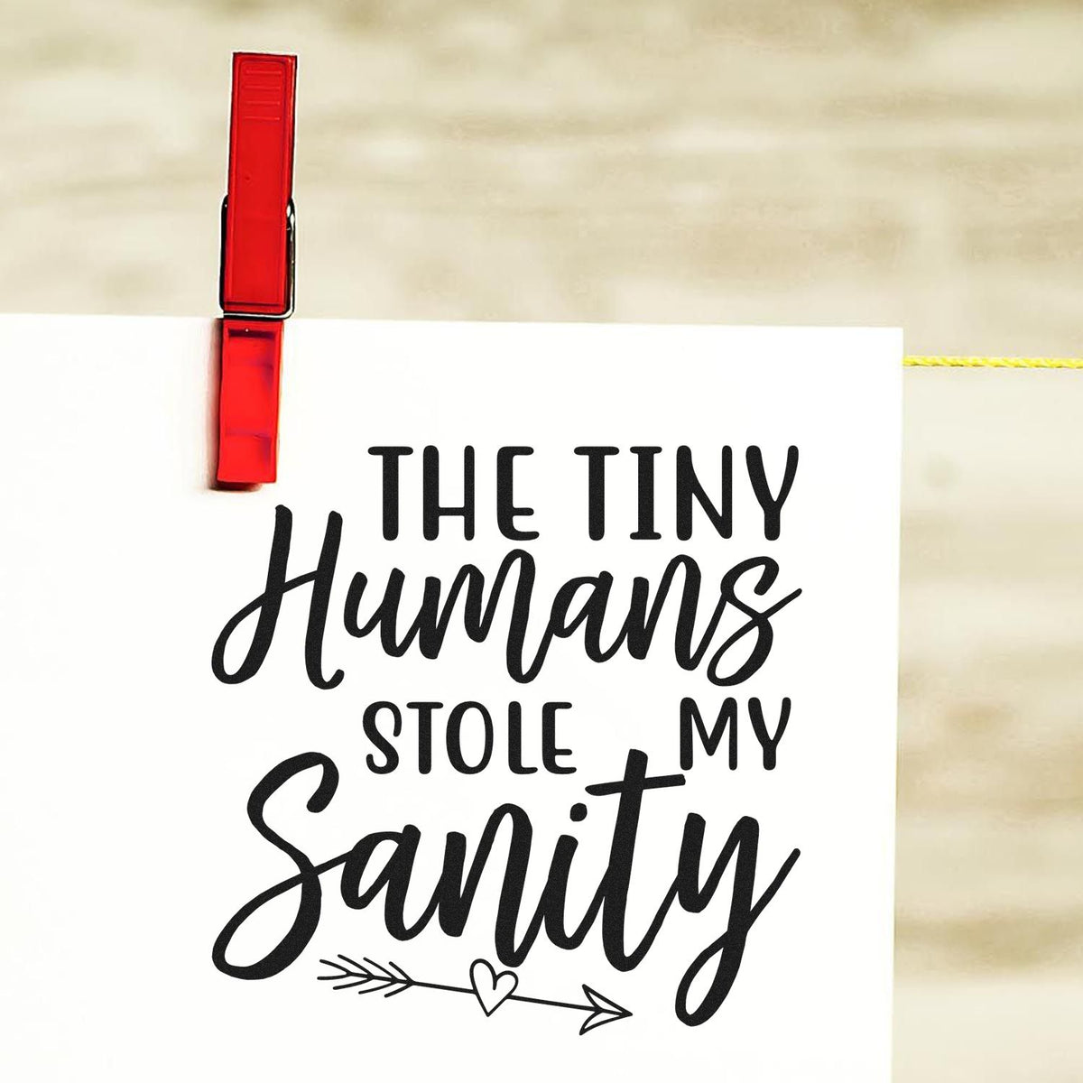 Red stamp clip holding a white stamped seal sign reading The Tiny Humans Stole My Sanity in black script.