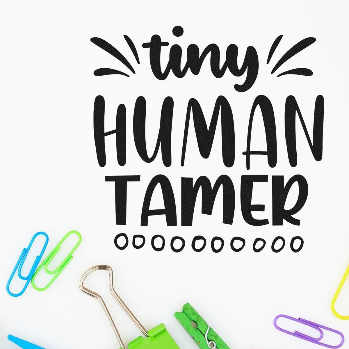 Black tiny HUMAN TAMER stamp and seal design on white, accented by colorful paper clips around the edges.