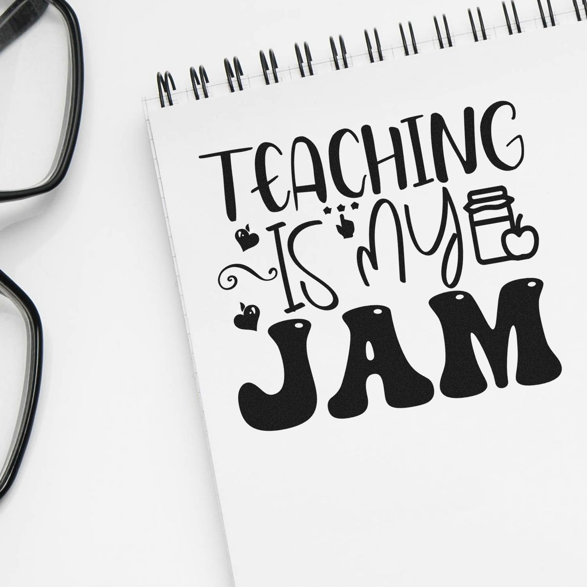 Black teacher stamp/seal design on white spiral notebook, reading Teaching is my JAM with hearts and apple accents.