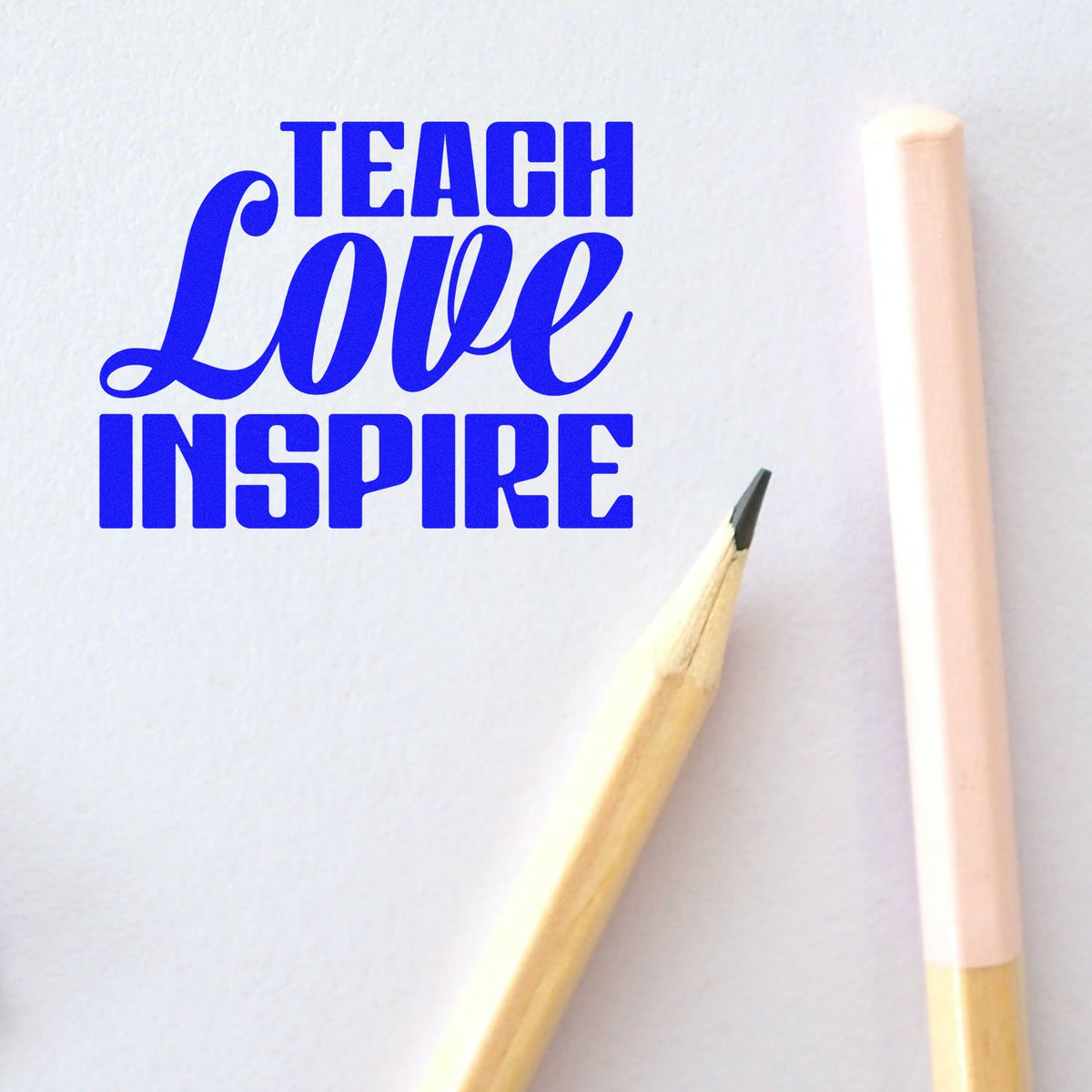 Blue Teach Love Inspire stamp and seal design on white paper, with a pencil and pastel pink pencil.