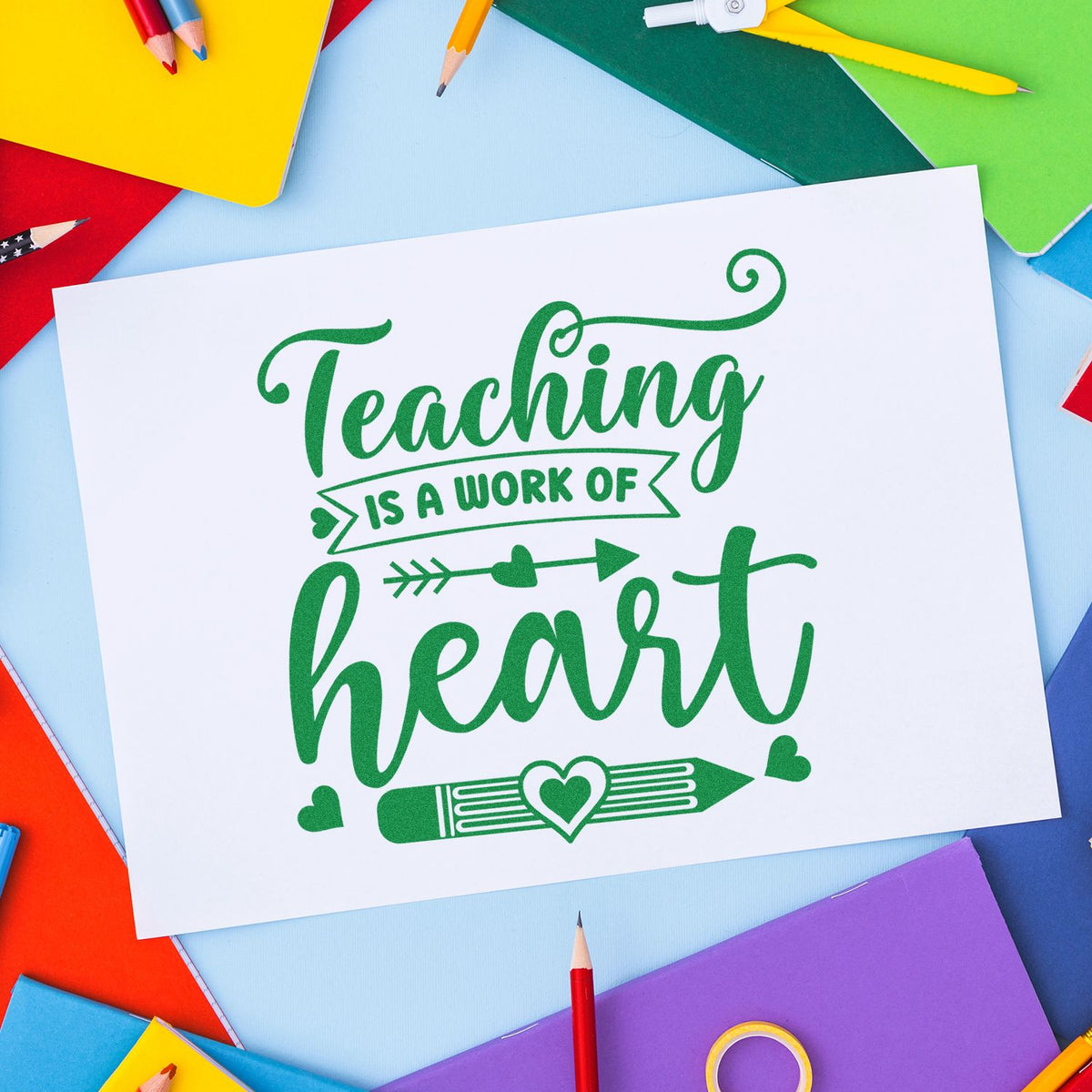 Green teaching heart stamp and seal design on white paper, surrounded by colorful pencils and notebooks.