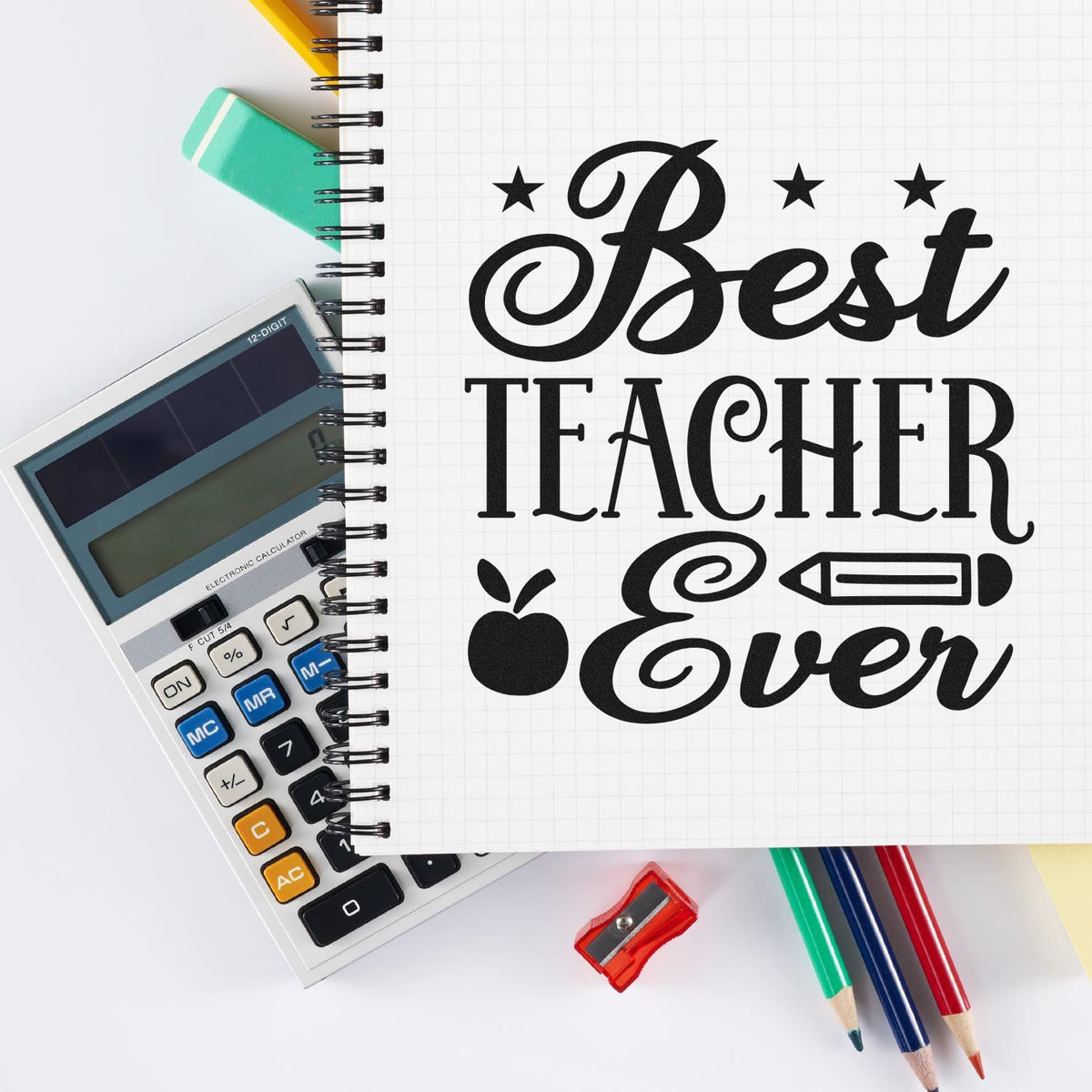 Black Best Teacher Ever stamp and seal on a spiral notebook with calculator, eraser, sharpener, and colored pencils.