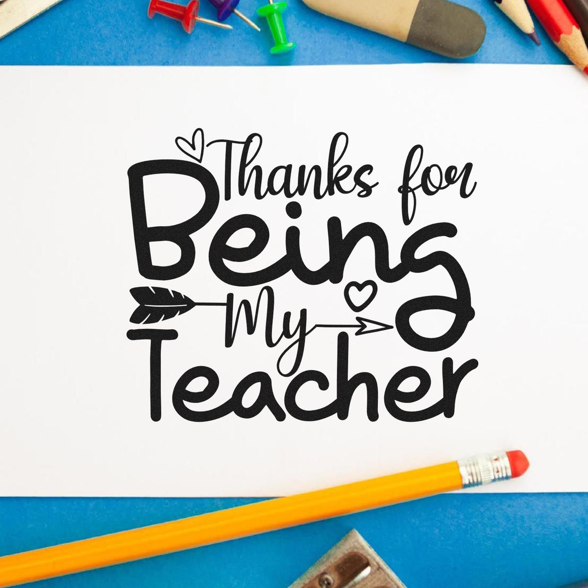 Black "Thanks for Being My Teacher" stamp design on white paper, with pencils and push pins on a blue background.
