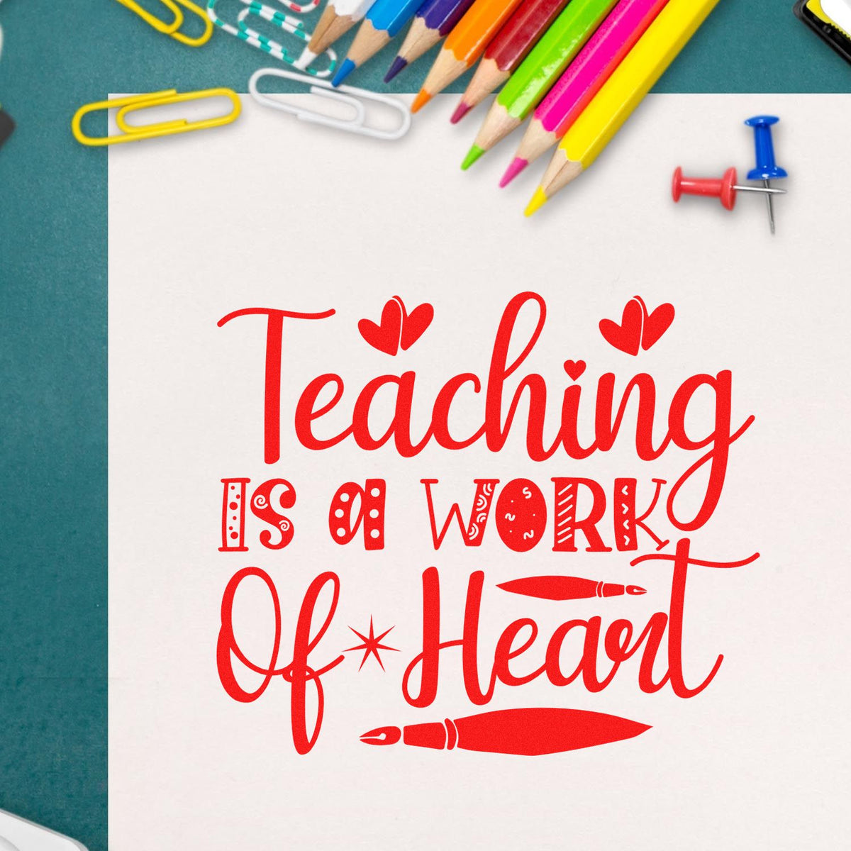 Red Teaching is a Work of Heart stamp and seal design on white paper, with colorful pencils, paper clips, and pushpins.