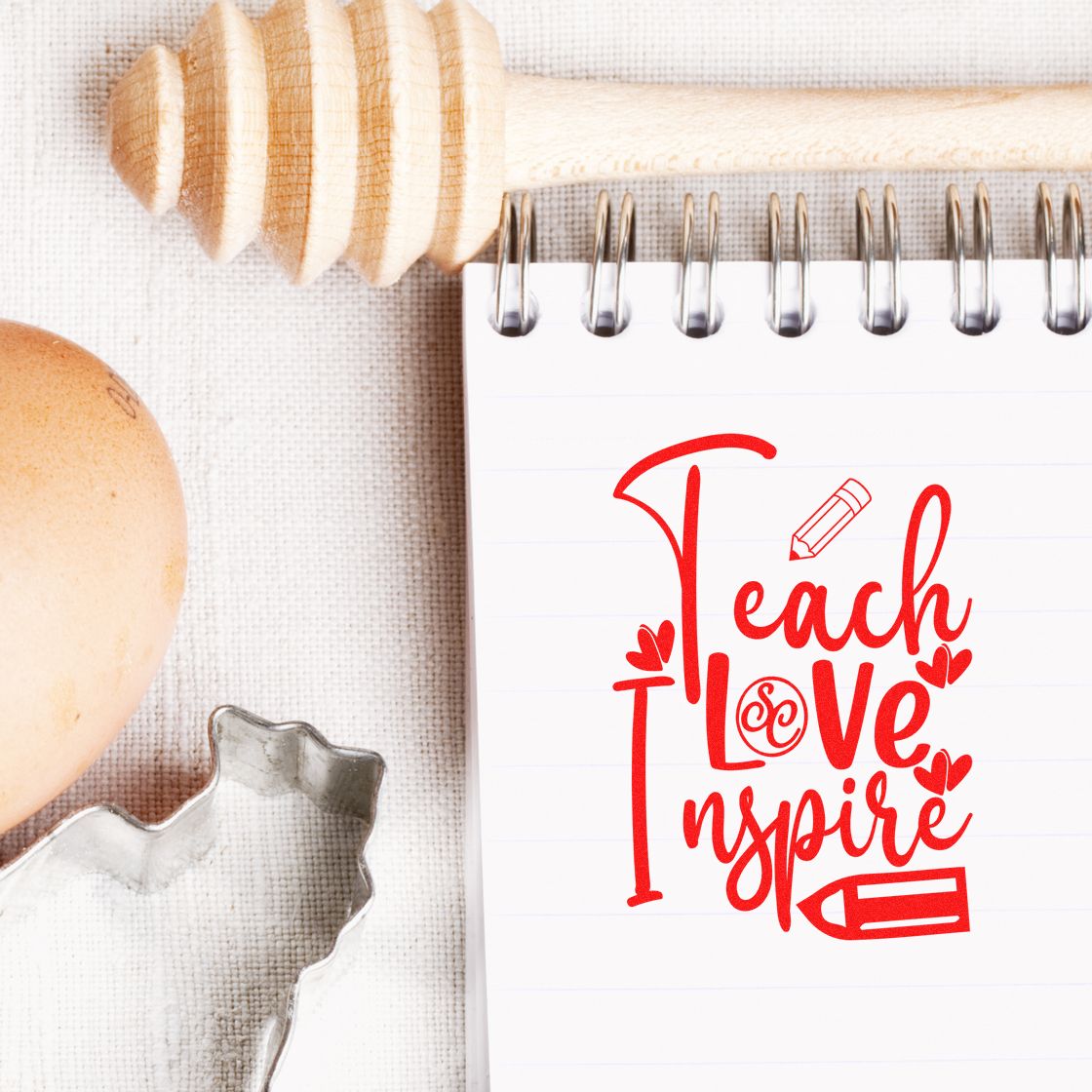 Red Teach Love Inspire stamp and seal design on white notepad, with wooden stamp handle and metal cutter.