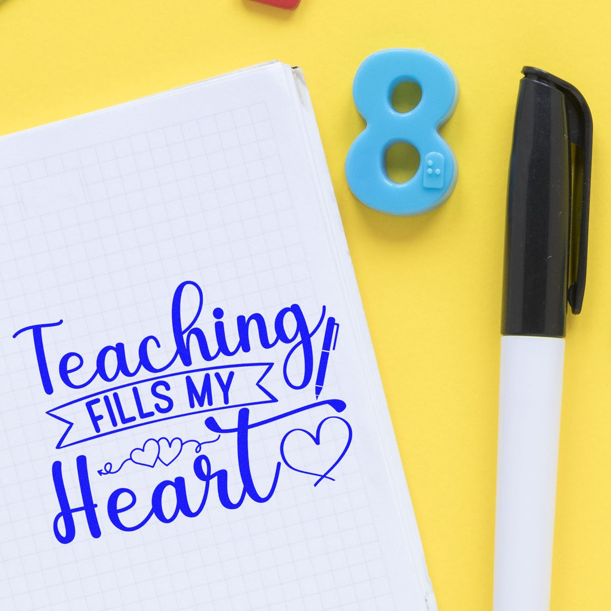Blue stamp and seal set, black-and-white pen, and notebook with Teaching fills my heart on yellow background.