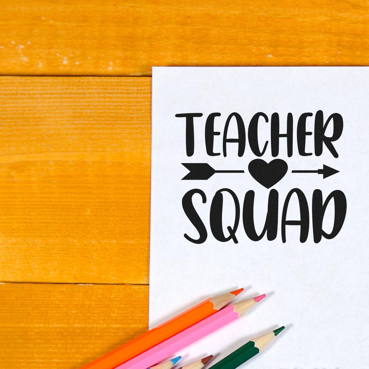 Black Teacher Squad stamp and seal design on white paper, with heart and arrows, on orange wood and colorful pencils.