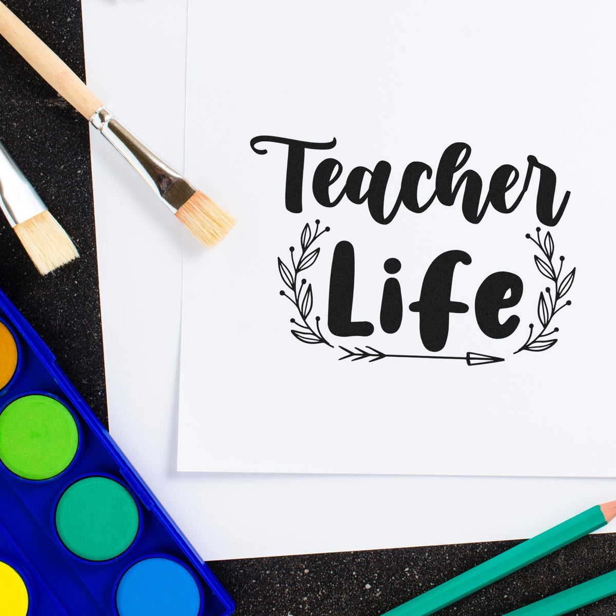Black Teacher Life stamp and seal design on white paper, with paintbrushes, watercolor paints, and teal pencils.