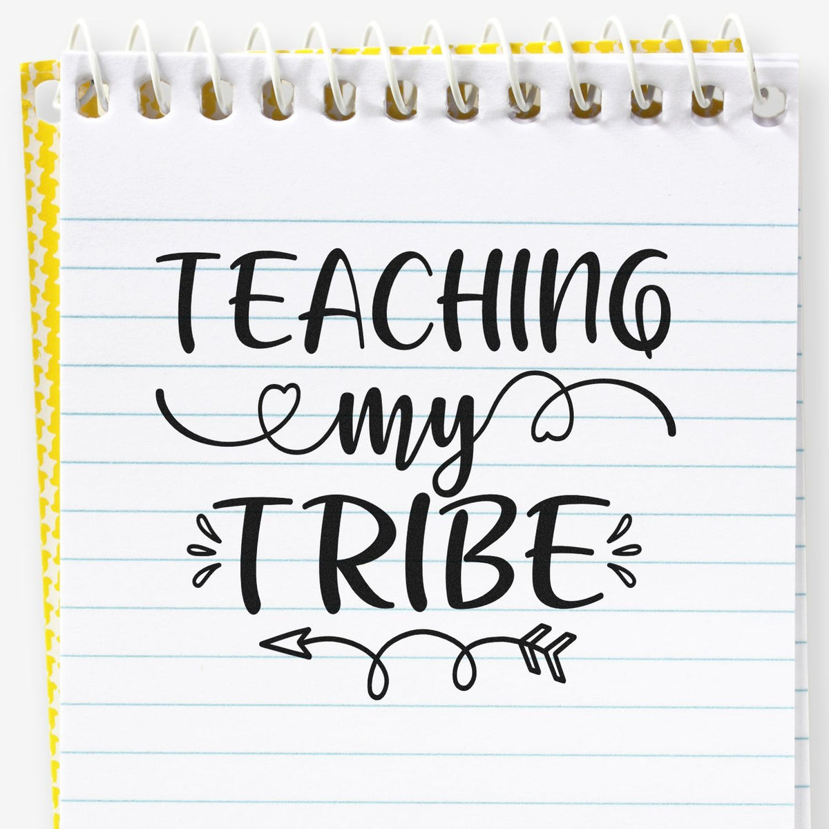 Black script teaching stamp reading Teaching my Tribe on white spiral notebook with light blue lines and yellow edge.