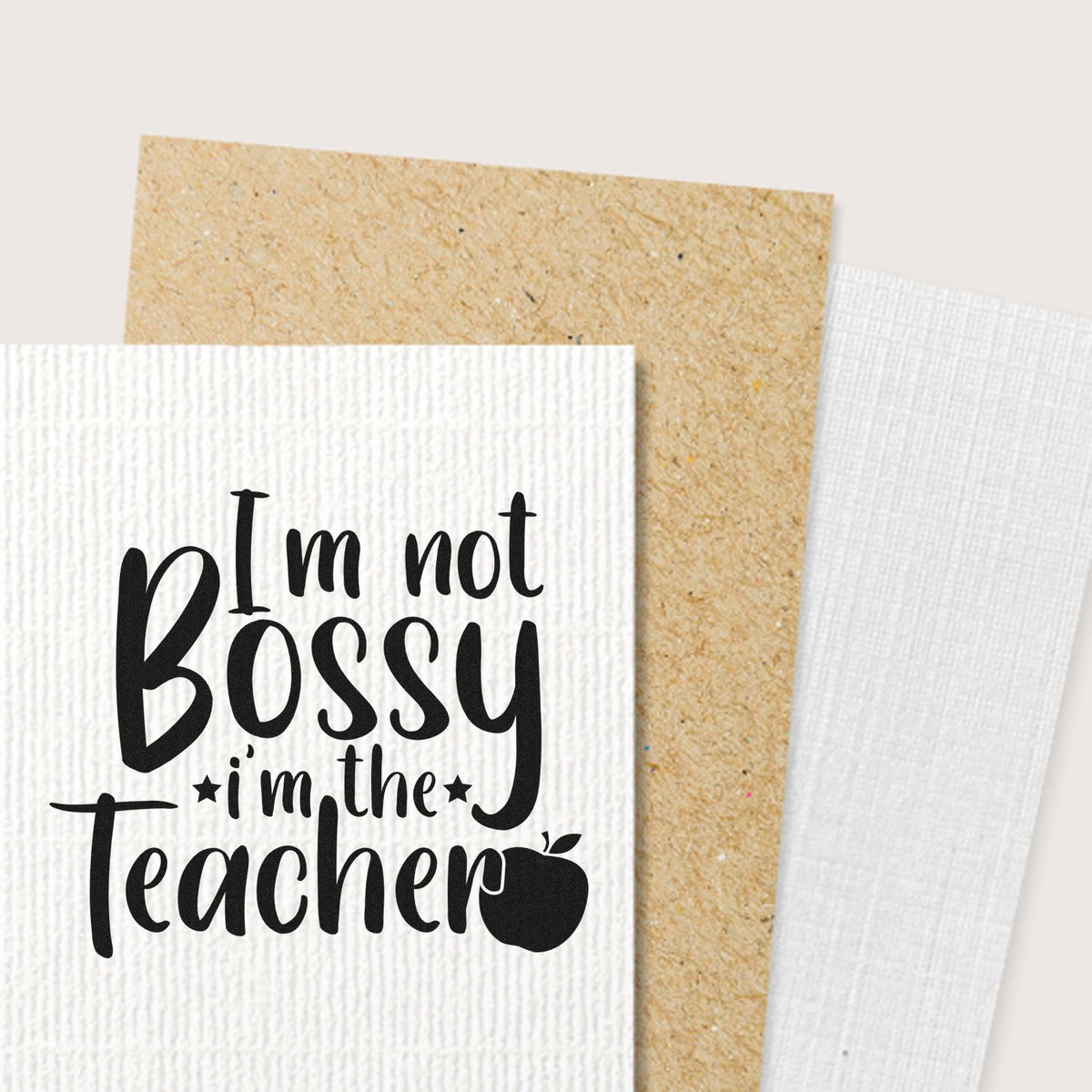 Black teacher stamp on white textured paper seal, reading Im not bossy, Im the teacher, with tan and white cards.