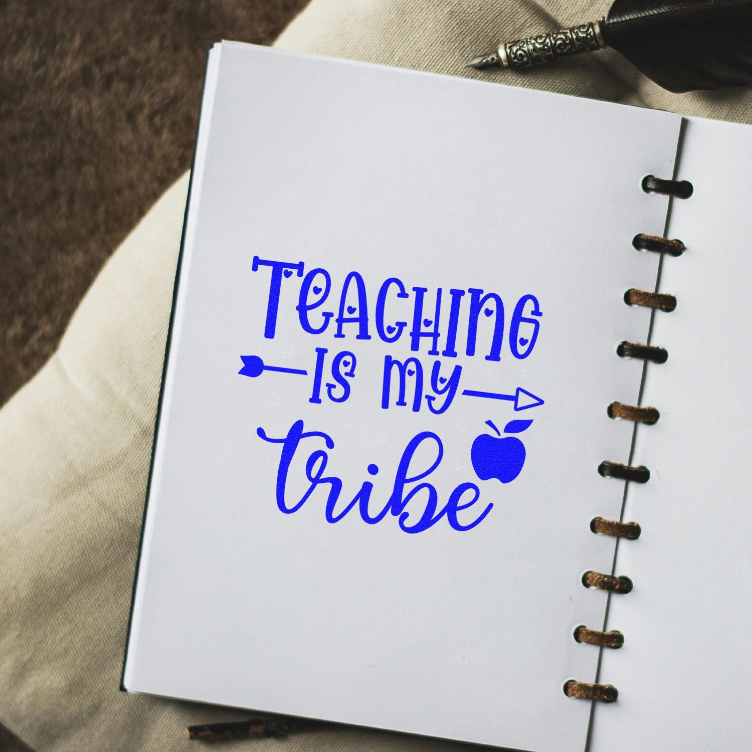 Blue teacher stamp design on a white notebook page, with brown spiral binding and a pen nearby.