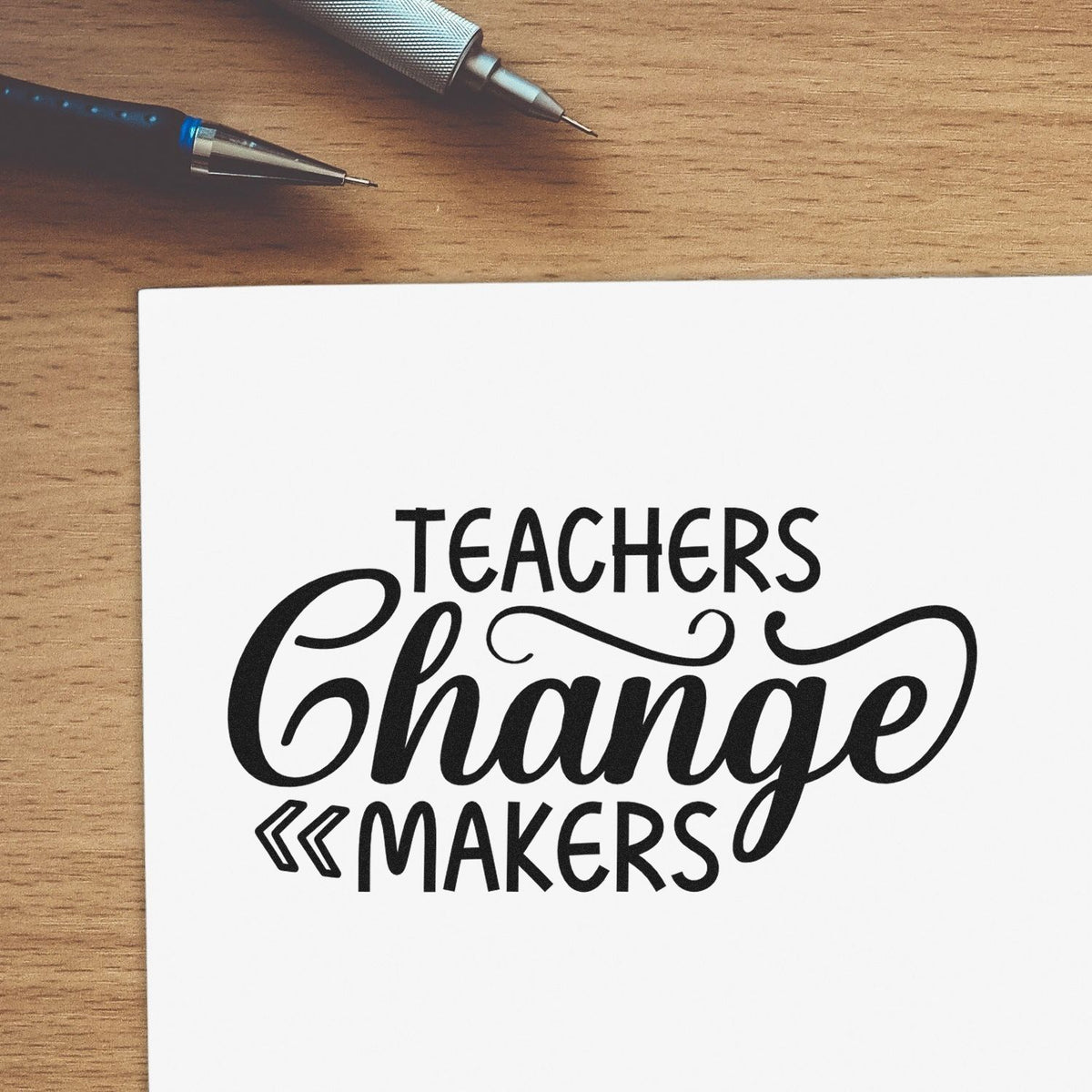 Black Teachers Change Makers stamp/seal design on white paper, with two pens on a wood desk.