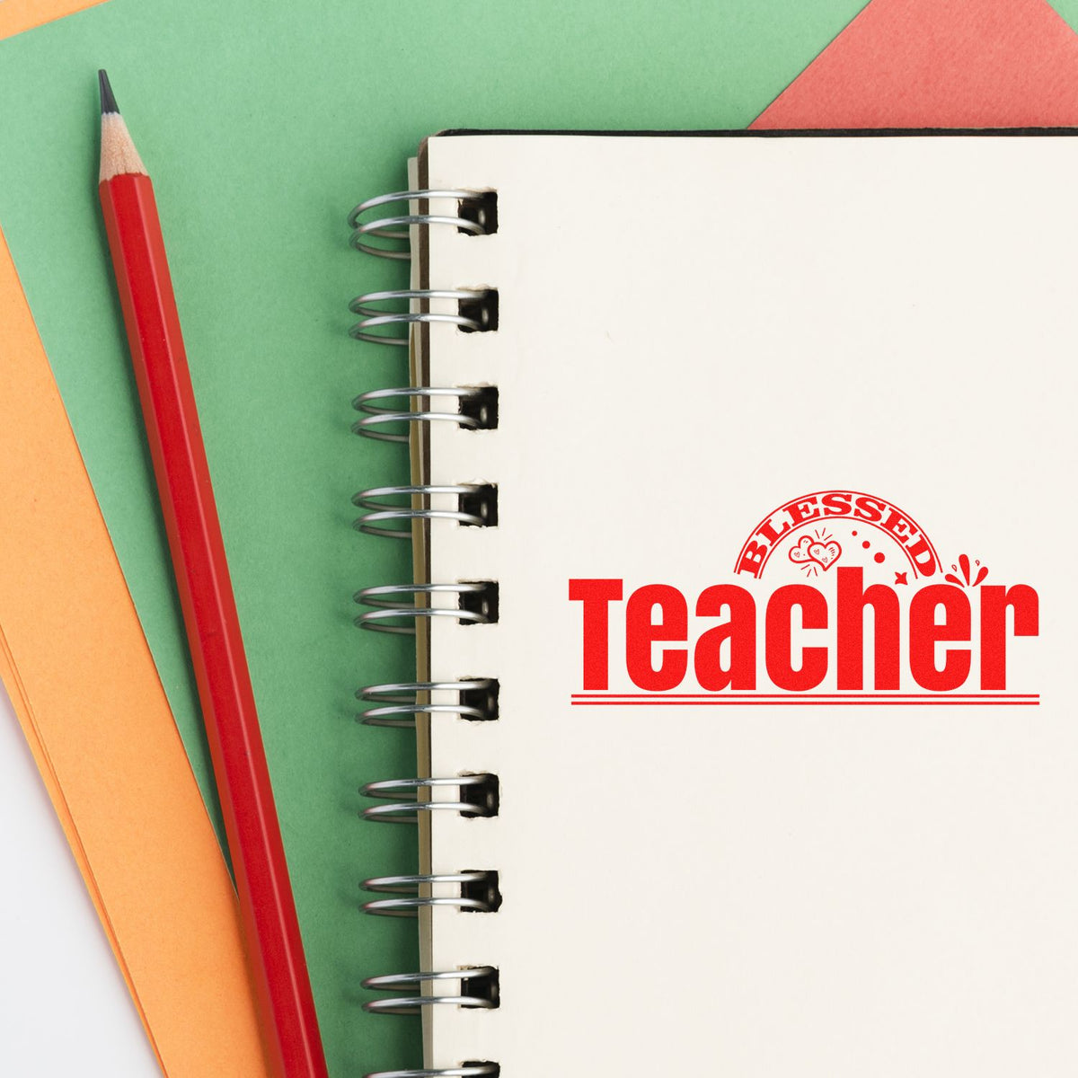 Red Blessed Teacher stamp seal on a spiral notebook, with a red pencil and green, orange paper background.