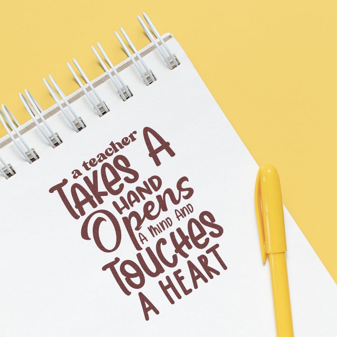 Brown teacher stamp on white spiral notebook with yellow pen and background, featuring a teacher quote.
