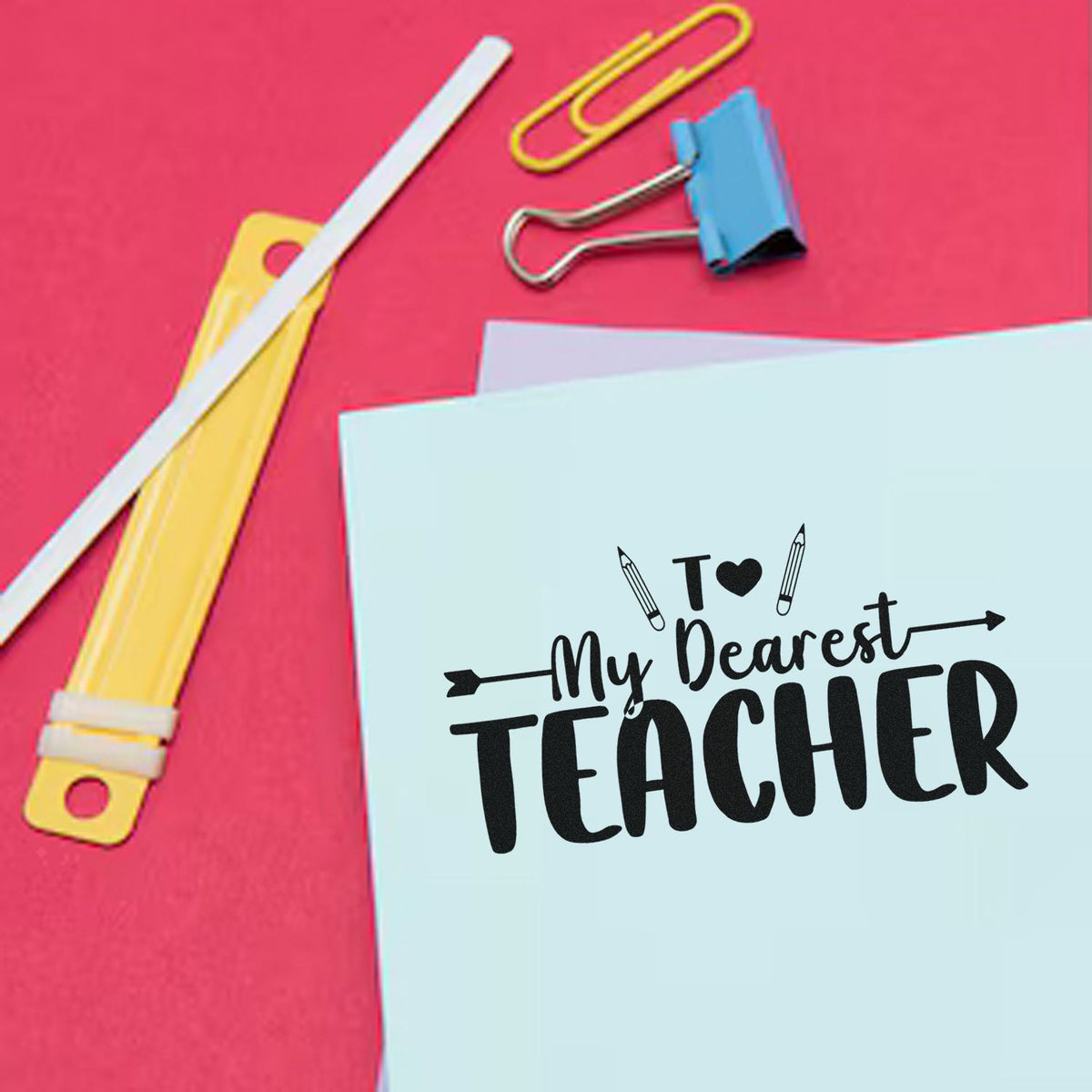 Teacher stamp seal reading To My Dearest Teacher on light blue card, with pink background and colorful binder clips.