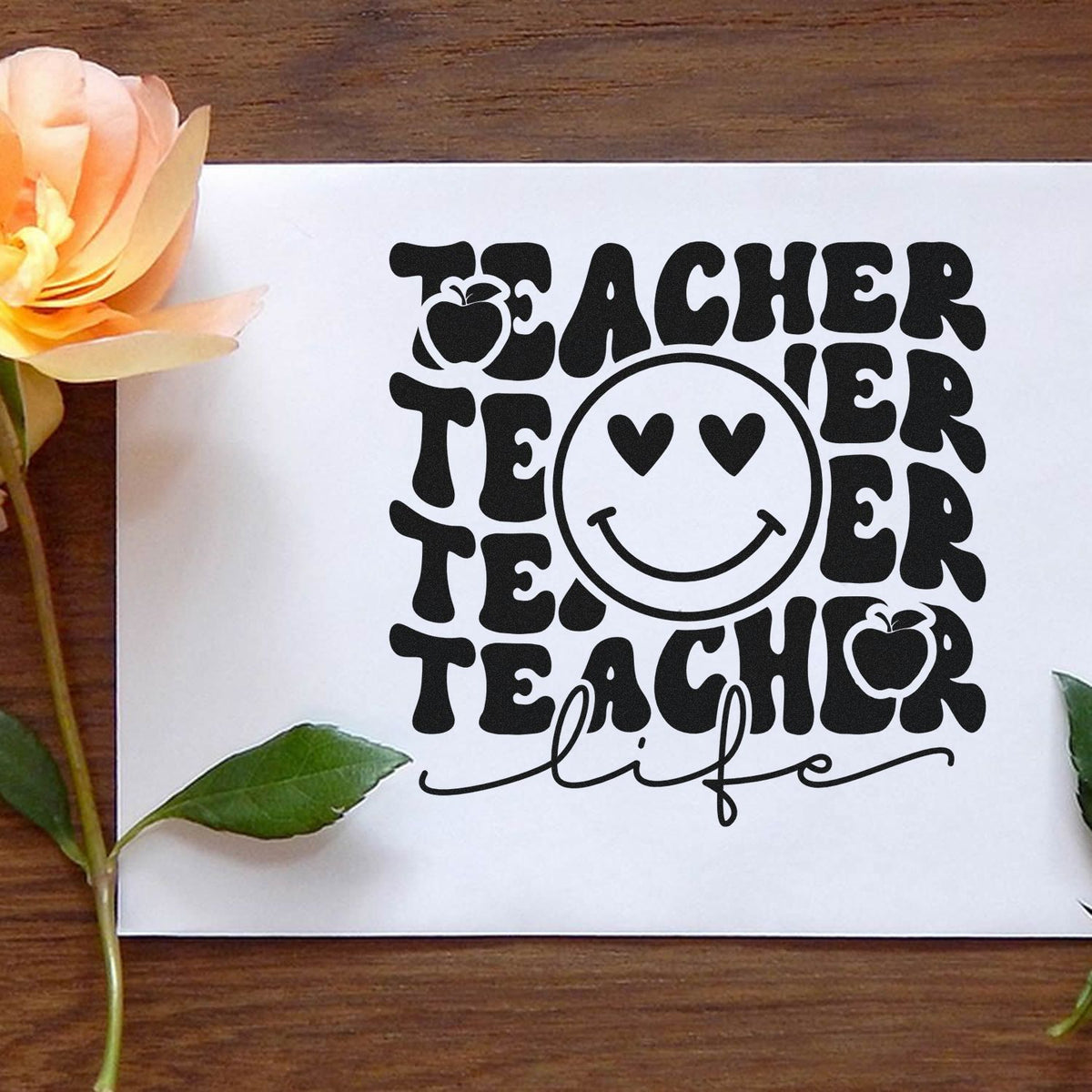 Black Teacher Life stamp and seal design with smiley face, apple icons, on a white sheet beside peach flower and green leaves.