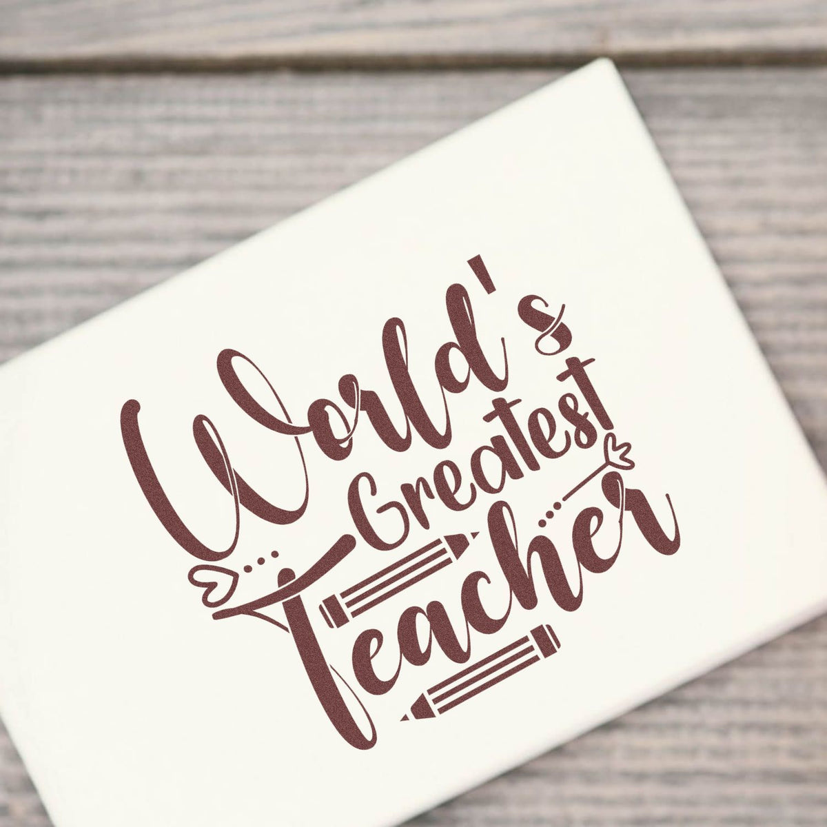 Cream custom stamp seal with maroon Worlds Greatest Teacher lettering and pencil graphics on rustic wood.