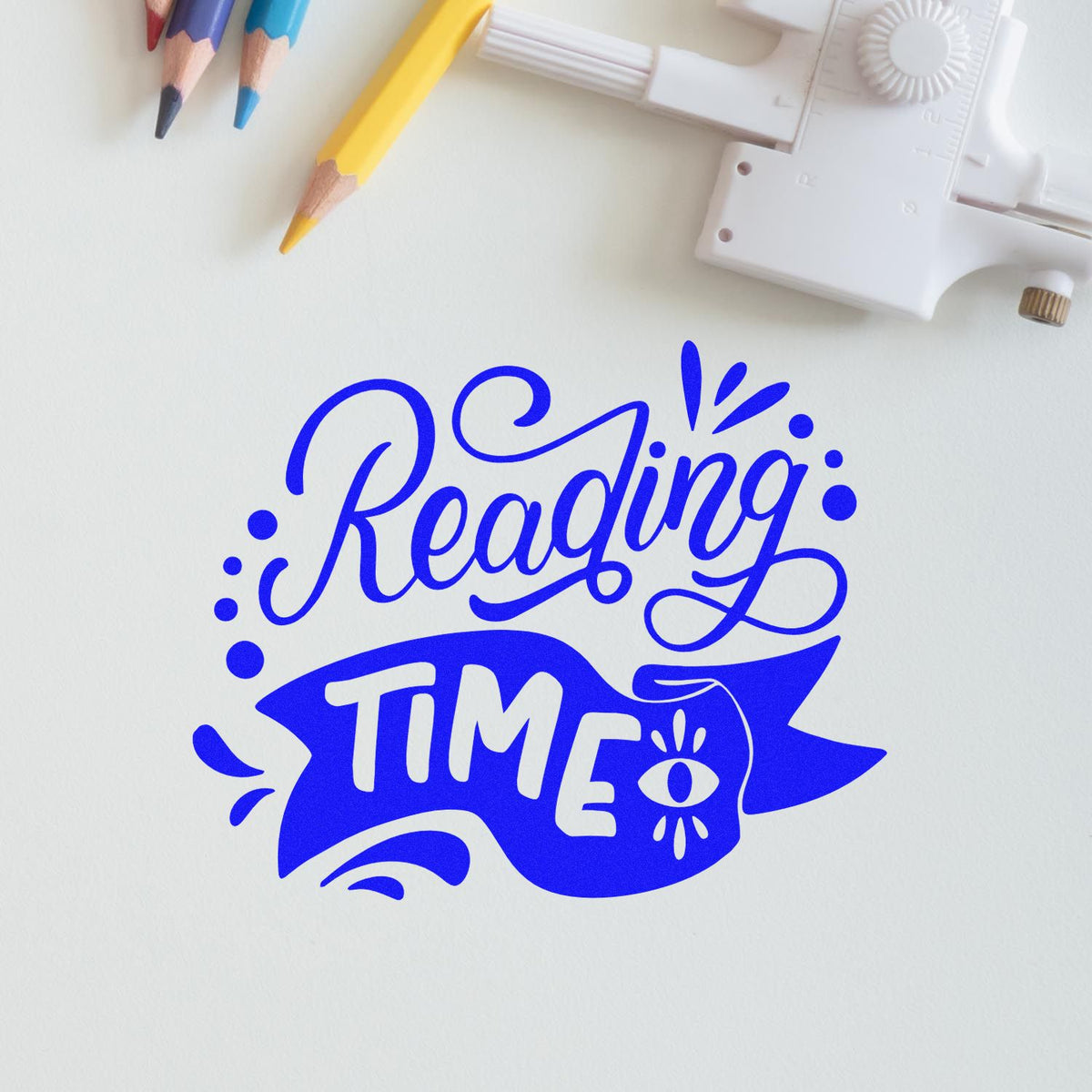 Blue Reading Time stamp design with eye icon on white paper, beside a white embossing seal tool and colored pencils.