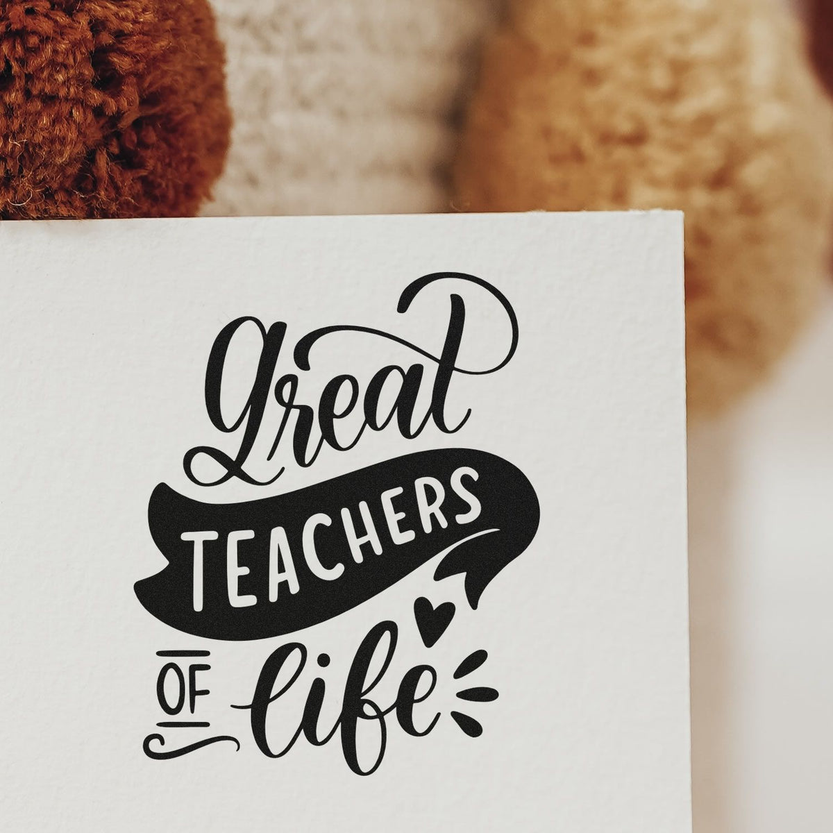 Black decorative stamp seal on white card reading Great Teachers of Life with heart accents.