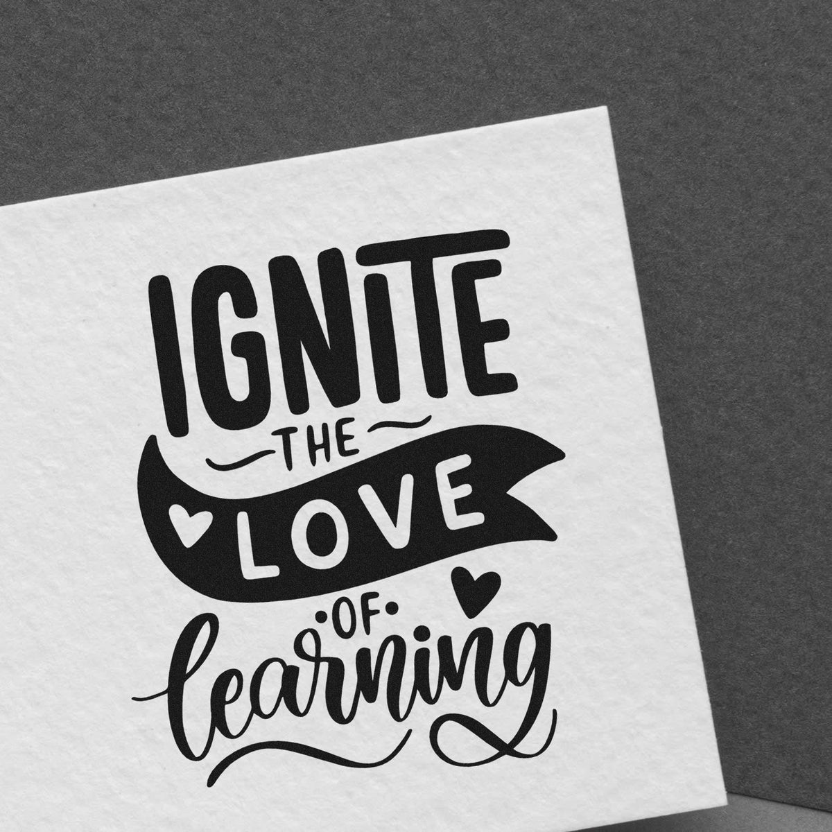 Black stamp/seal design on white paper reading Ignite the love of learning with hearts and decorative script.