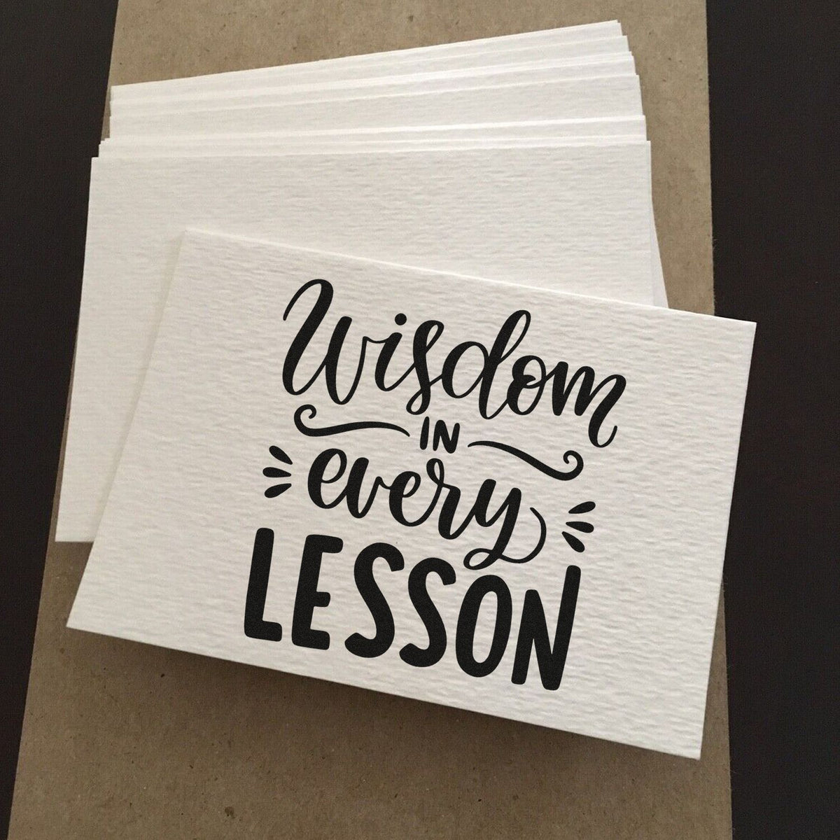 White stamp and seal sheets stacked on brown backing, featuring black Wisdom in every lesson lettering.