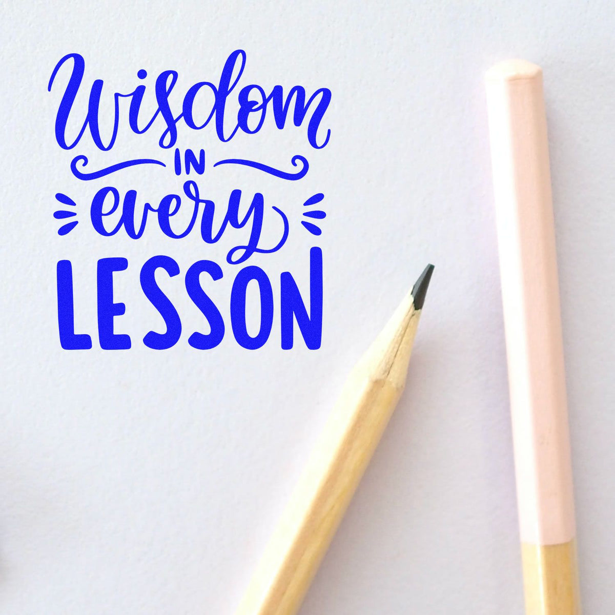 Blue Wisdom in every Lesson lettering on white paper with a wooden pencil and pastel pink stamp/seal tool.