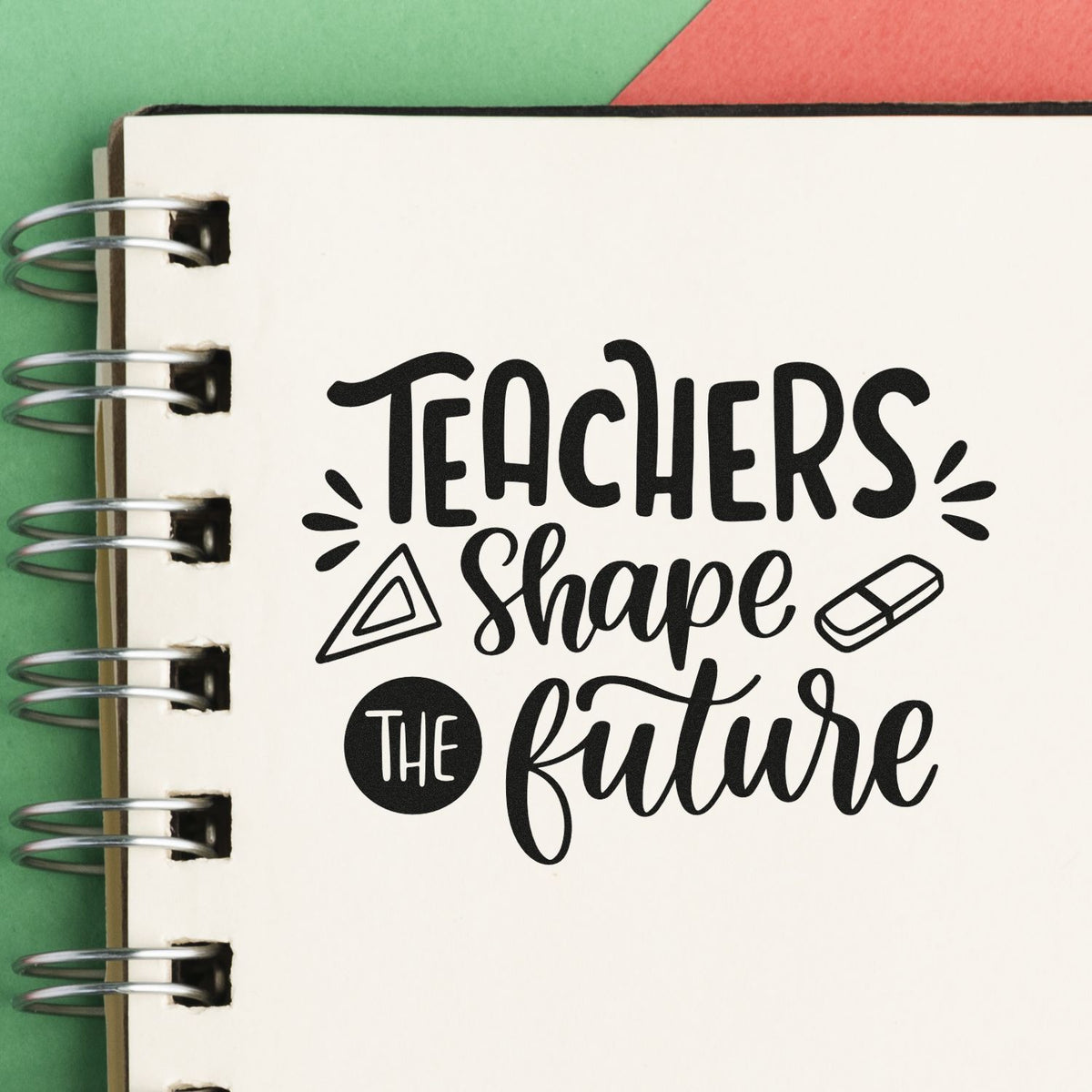 Black teacher stamp and seal design on a white spiral notebook page, with green and red background and metal rings.
