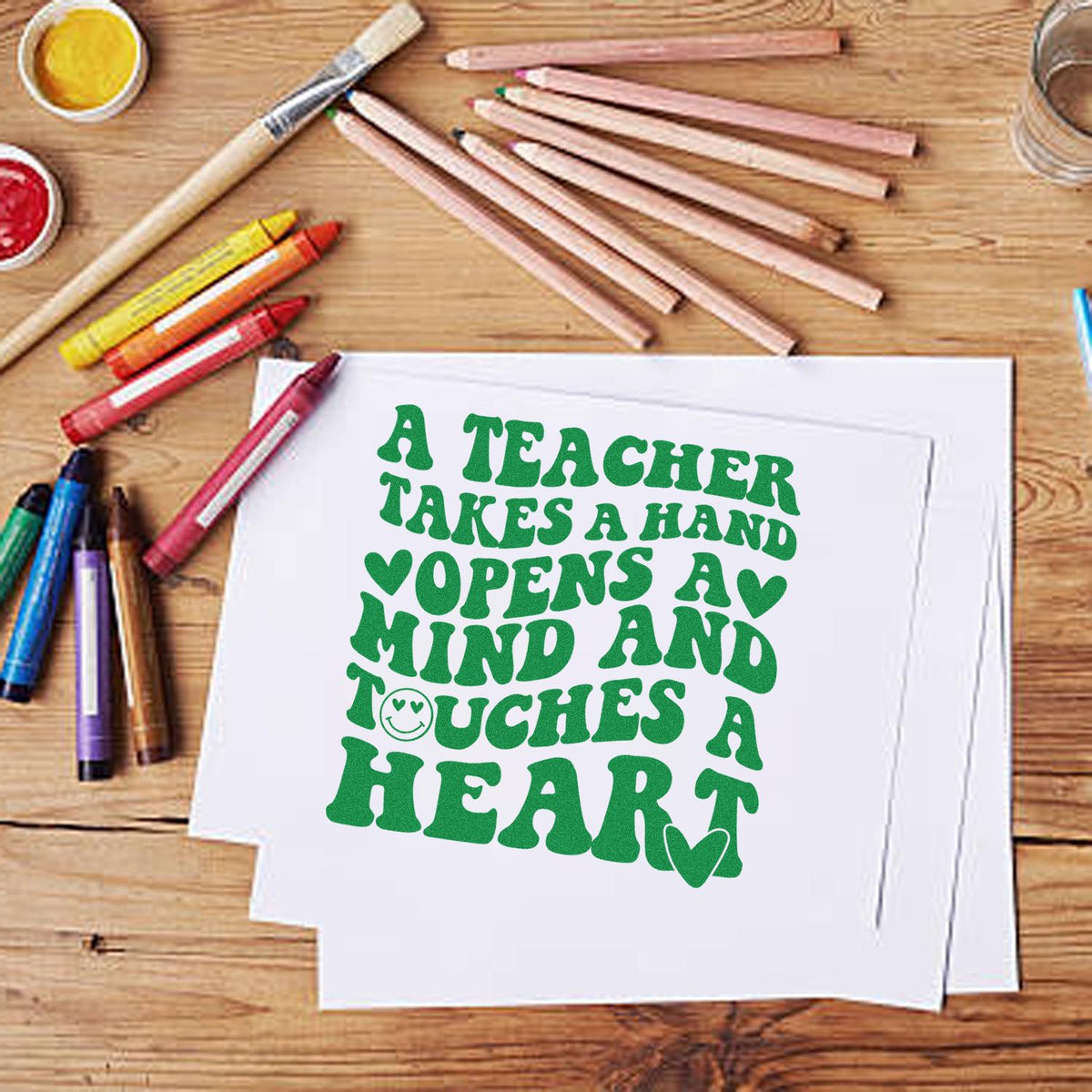 Green teacher appreciation stamp and seal design on white paper, with colored pencils, brushes, and seal supplies on a wood table.