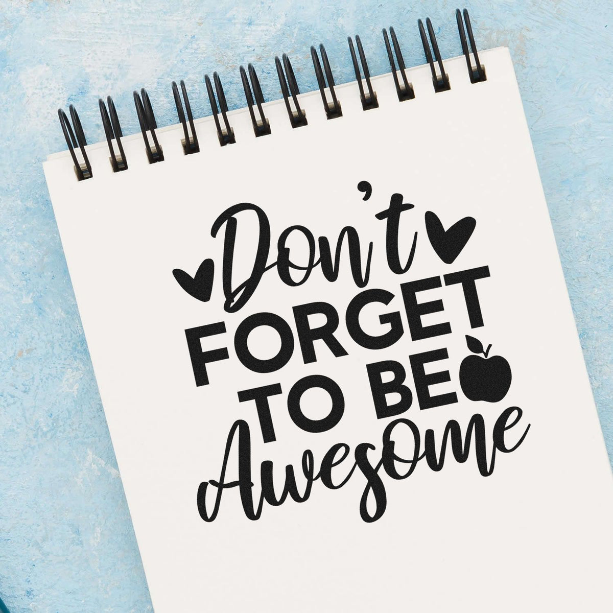 Black stamp/seal design on white spiral notepad: Dont forget to be Awesome with hearts and apple on blue background.