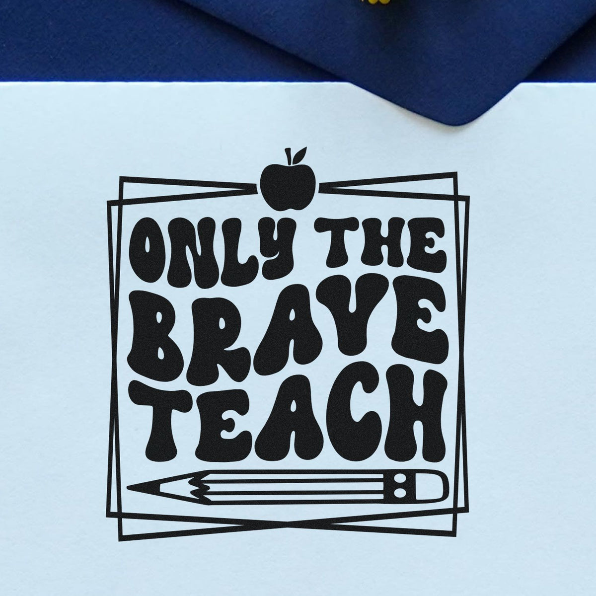 Black teacher stamp/seal design with apple and pencil, reading Only the Brave Teach on white paper with navy fabric background.