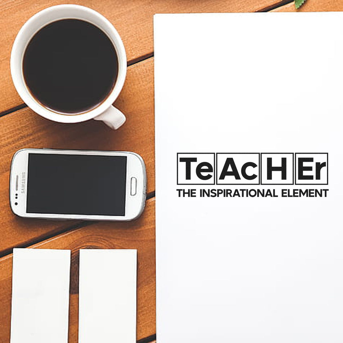 Teacher stamp and seal products with black logo on white sheet, beside coffee, smartphone, and blank cards on a wooden desk.