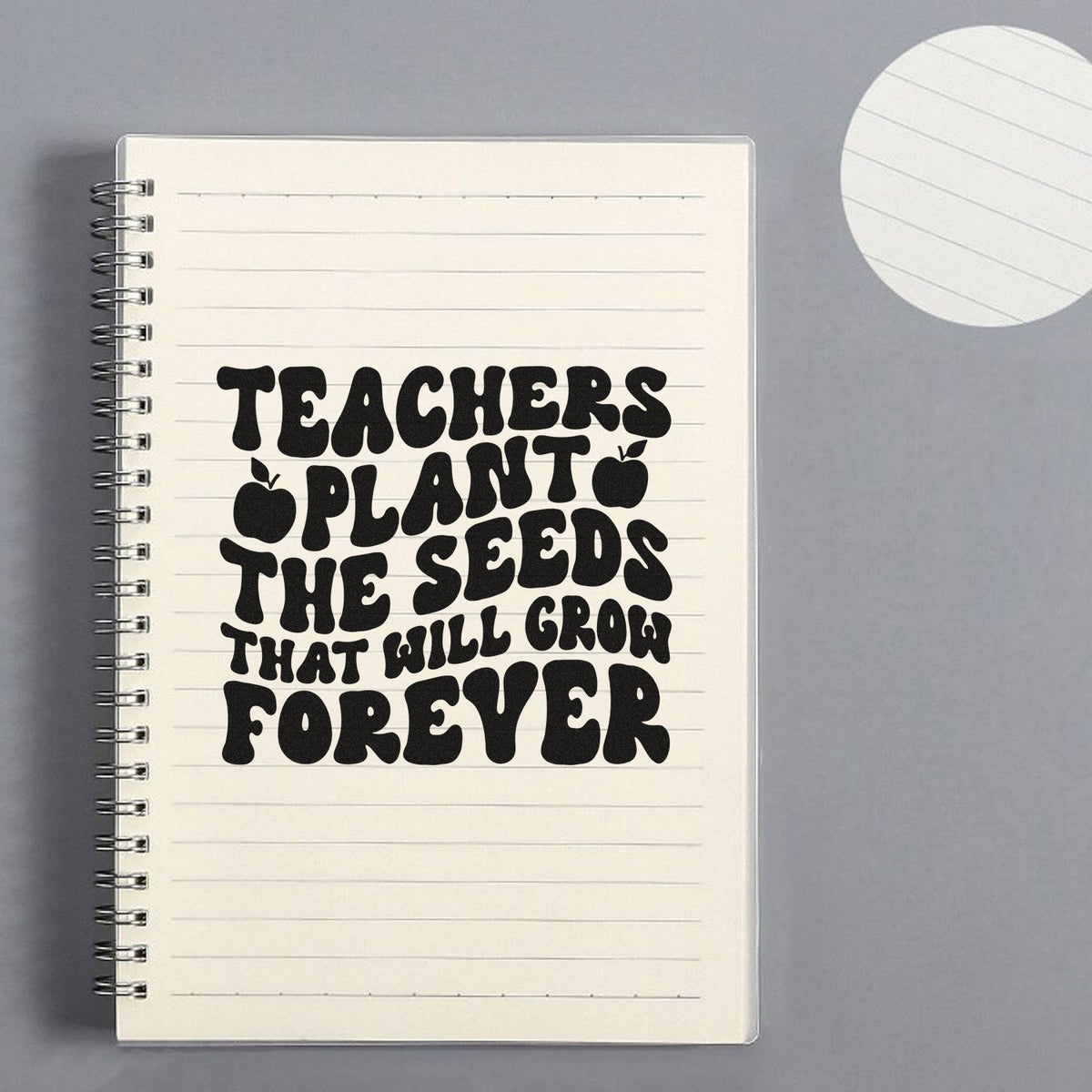Black teacher plant seed forever rubber stamp design on cream lined notebook, with apple icons and spiral binding.