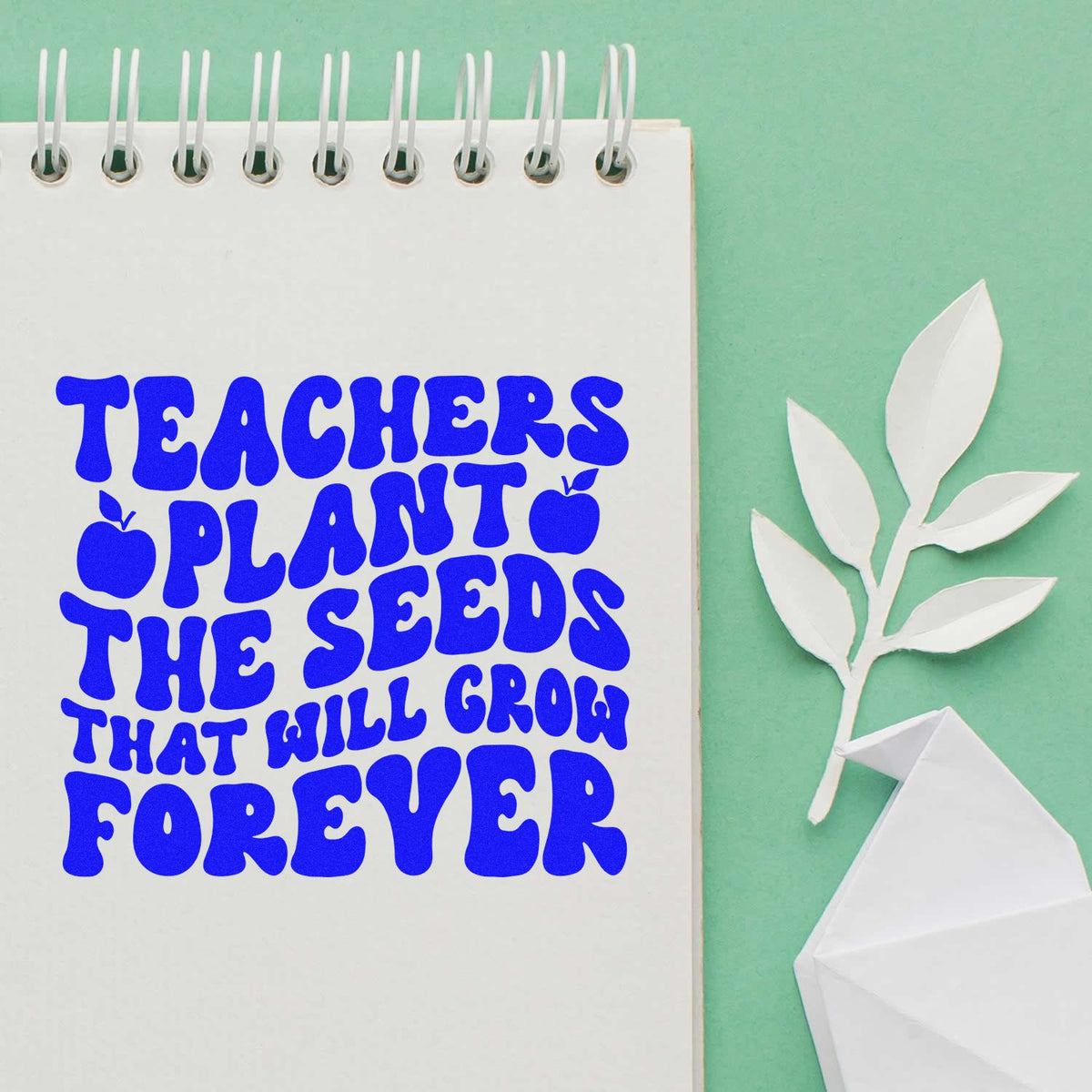Blue teacher quote stamp on white spiral notebook, with white paper leaf seal and folded paper accent on mint green background.