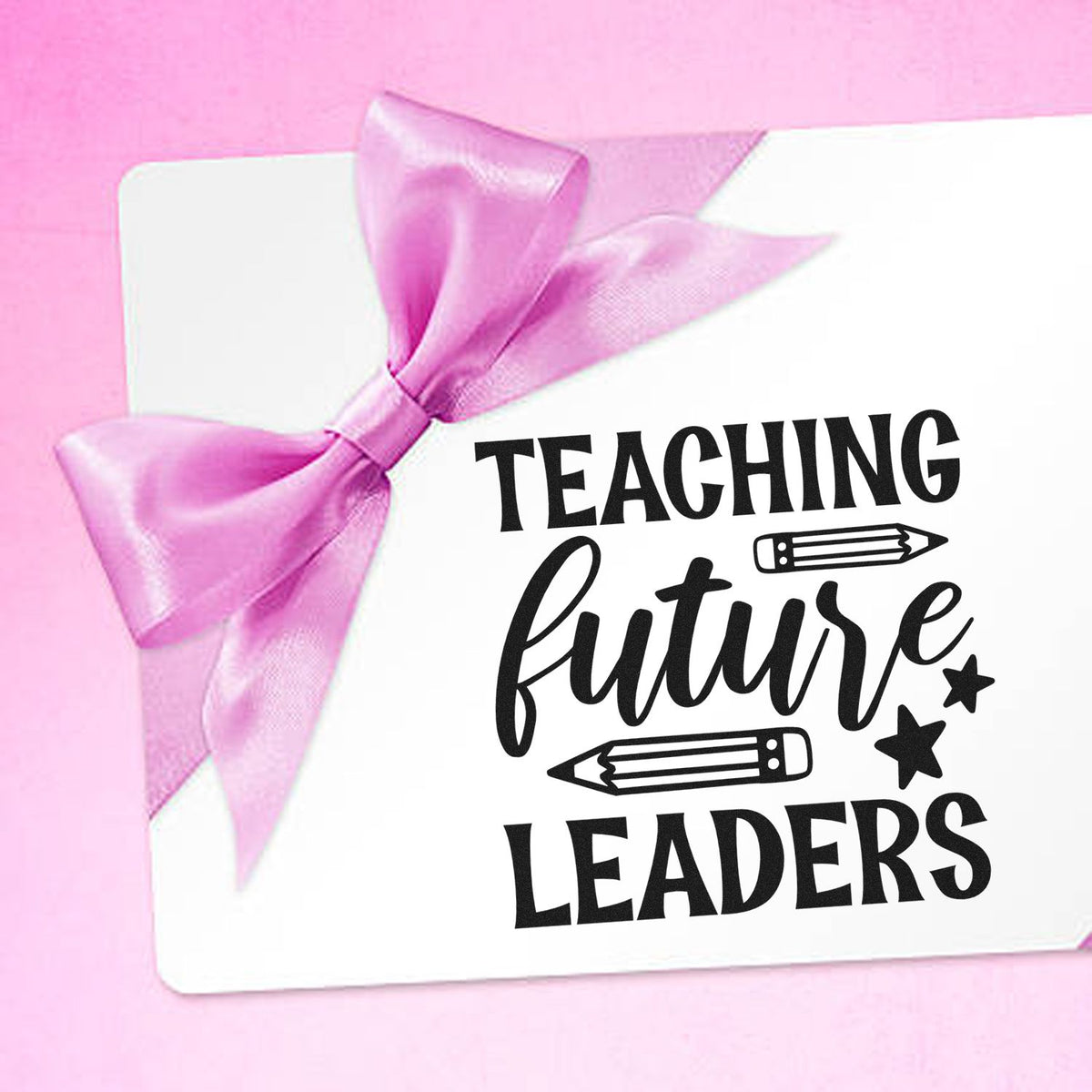 White teacher stamp seal with pink satin bow and black Teaching Future Leaders text, pencils, and stars on pink.